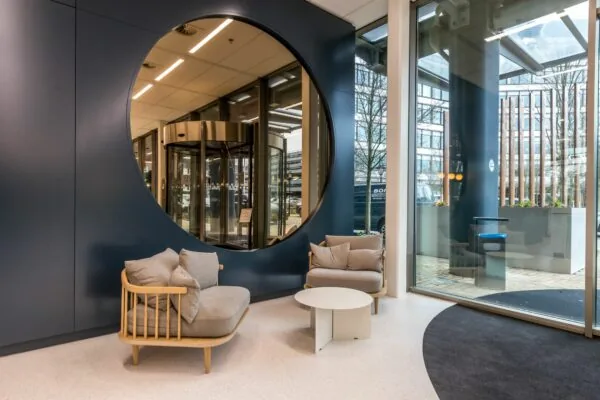 Moderne wachtruimte bij Vliegend Hertlaan 21 met designstoelen, ronde spiegelwand en uitzicht op de entree.