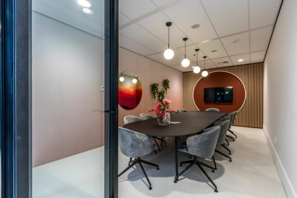 Moderne vergaderruimte aan de Vliegend Hertlaan 21 met ovale tafel, grijze stoelen, wanddecoratie en een ronde houten accentmuur met tv.