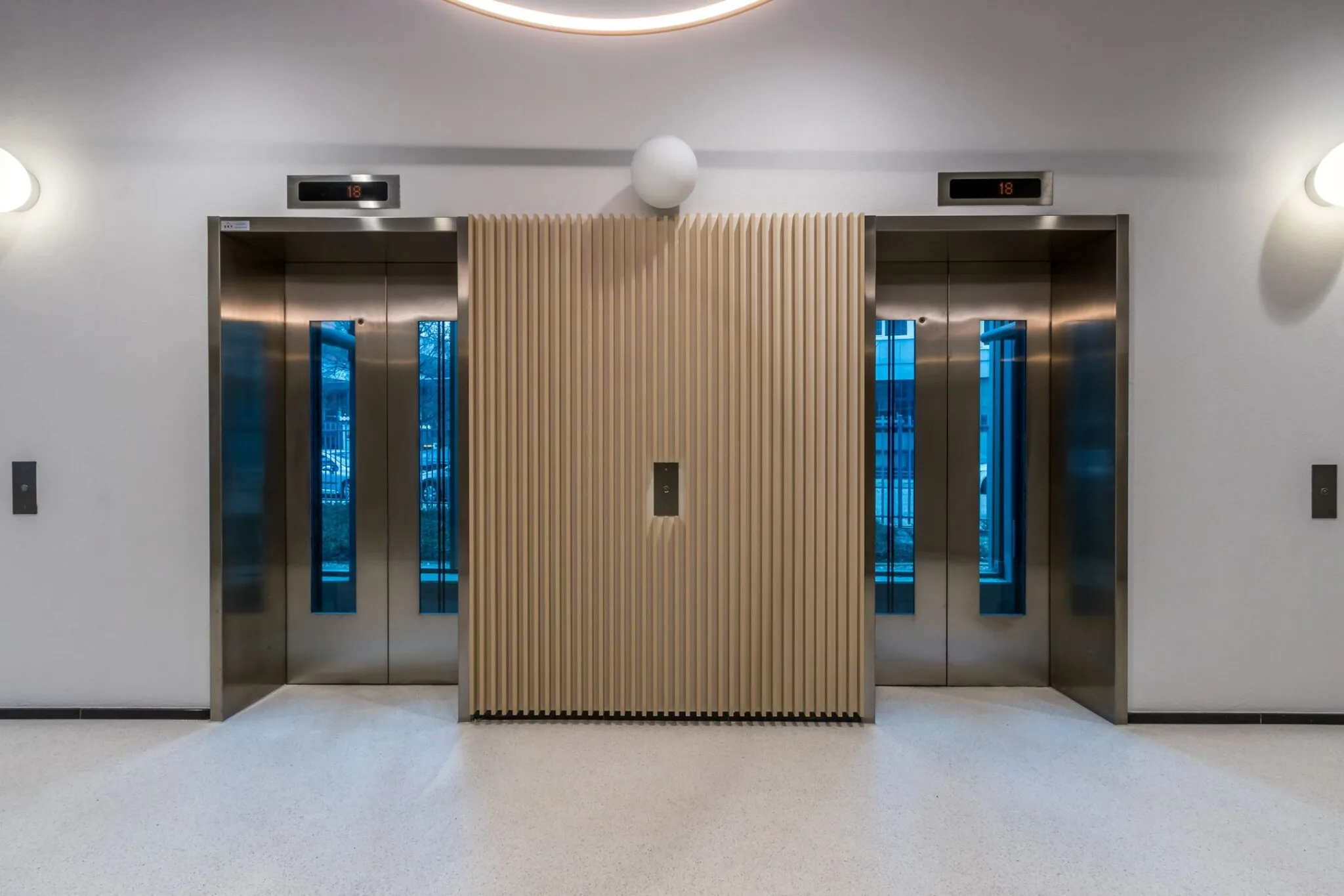 Twee gesloten liften met roestvrijstalen deuren in de hal van Vliegend Hertlaan 21, met een licht houten tussenwand.