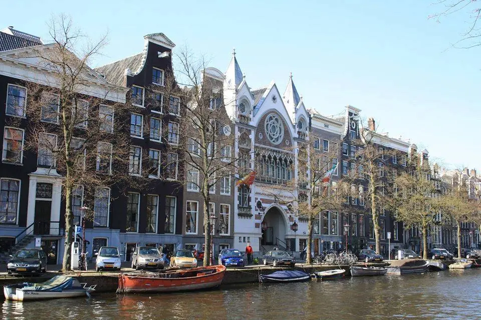 Vooraanzicht van het karakteristieke Felix Meritis-gebouw aan een Amsterdamse gracht met boten en historische gevels.