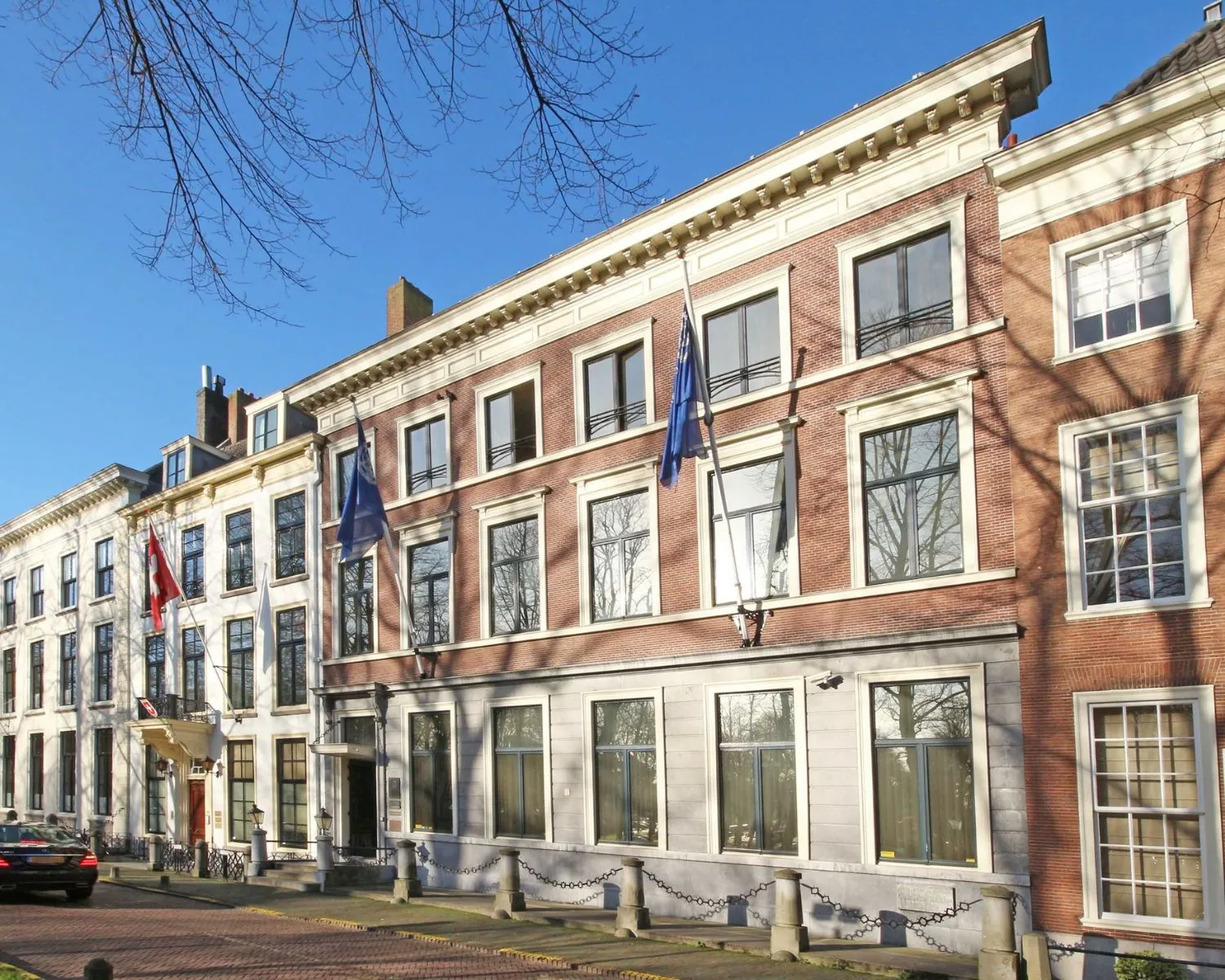 Vooraanzicht van een statig herenhuis met vlaggen aan de gevel in een historische straat.