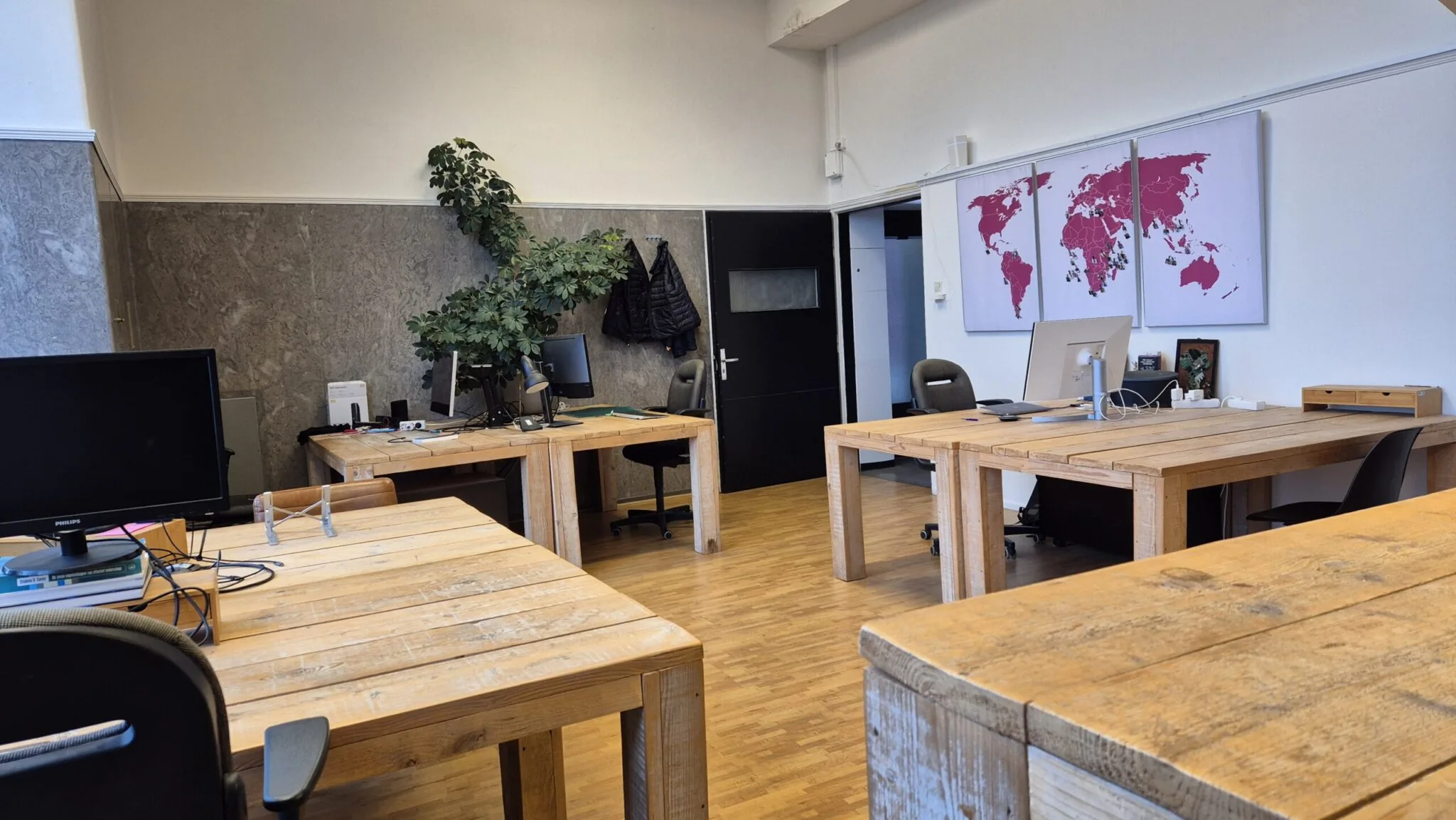 Kantoorruimte in WG-plein 100 unit 478 met houten bureaus, computers, een wereldkaart aan de muur en een grote kamerplant.