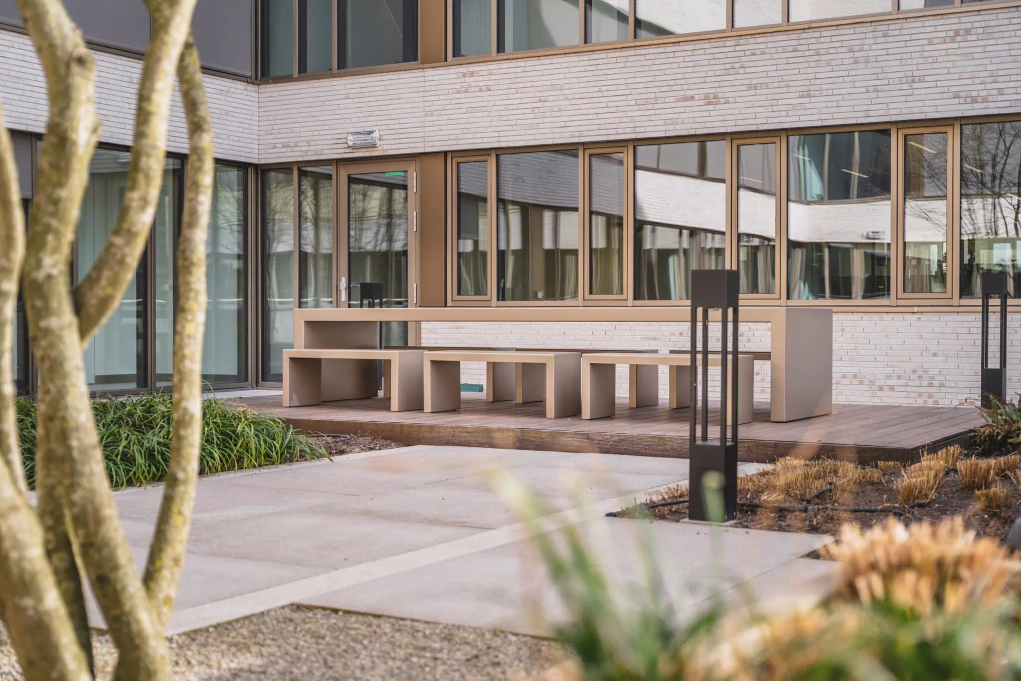 Moderne buitentafel met bijpassende banken op een houten terras in een verzorgde binnenplaats van gebouw Walborg.