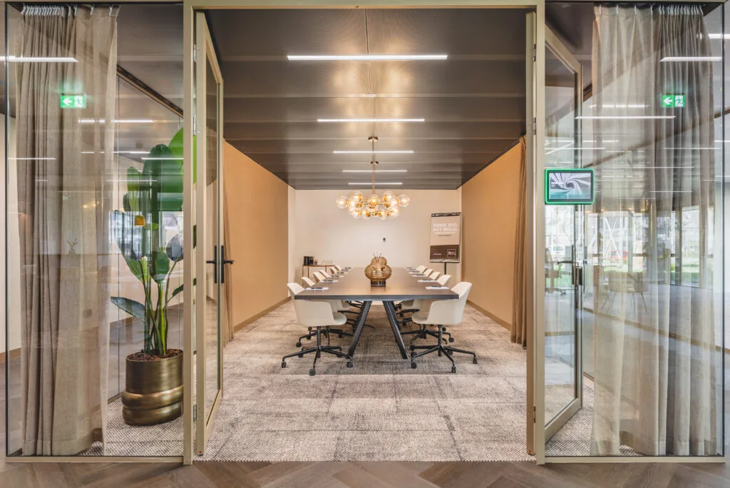 Vergaderruimte Walborg 2.4 met een lange tafel, moderne stoelen, glazen deuren en warme verlichting.