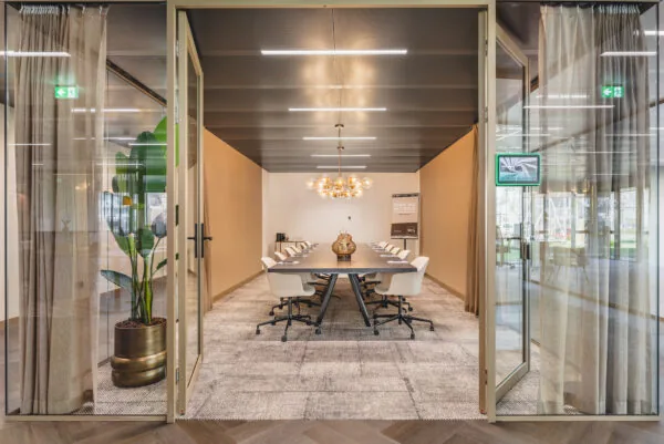 Vergaderruimte Walborg 2.4 met een lange tafel, moderne stoelen, glazen deuren en warme verlichting.