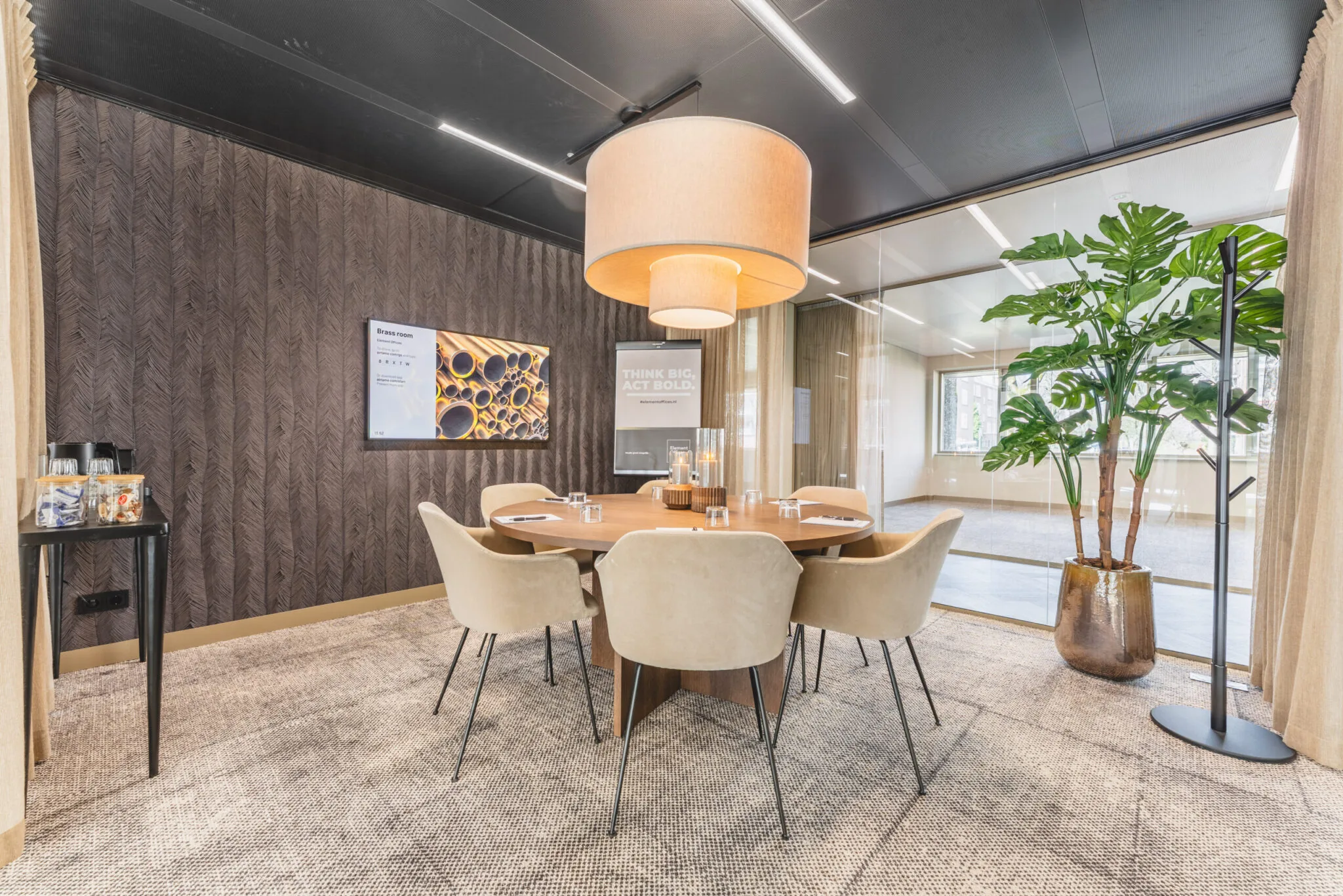 Vergaderruimte Walborg 2.6 met ronde tafel, zes beige stoelen, grote hanglamp en glazen wand.