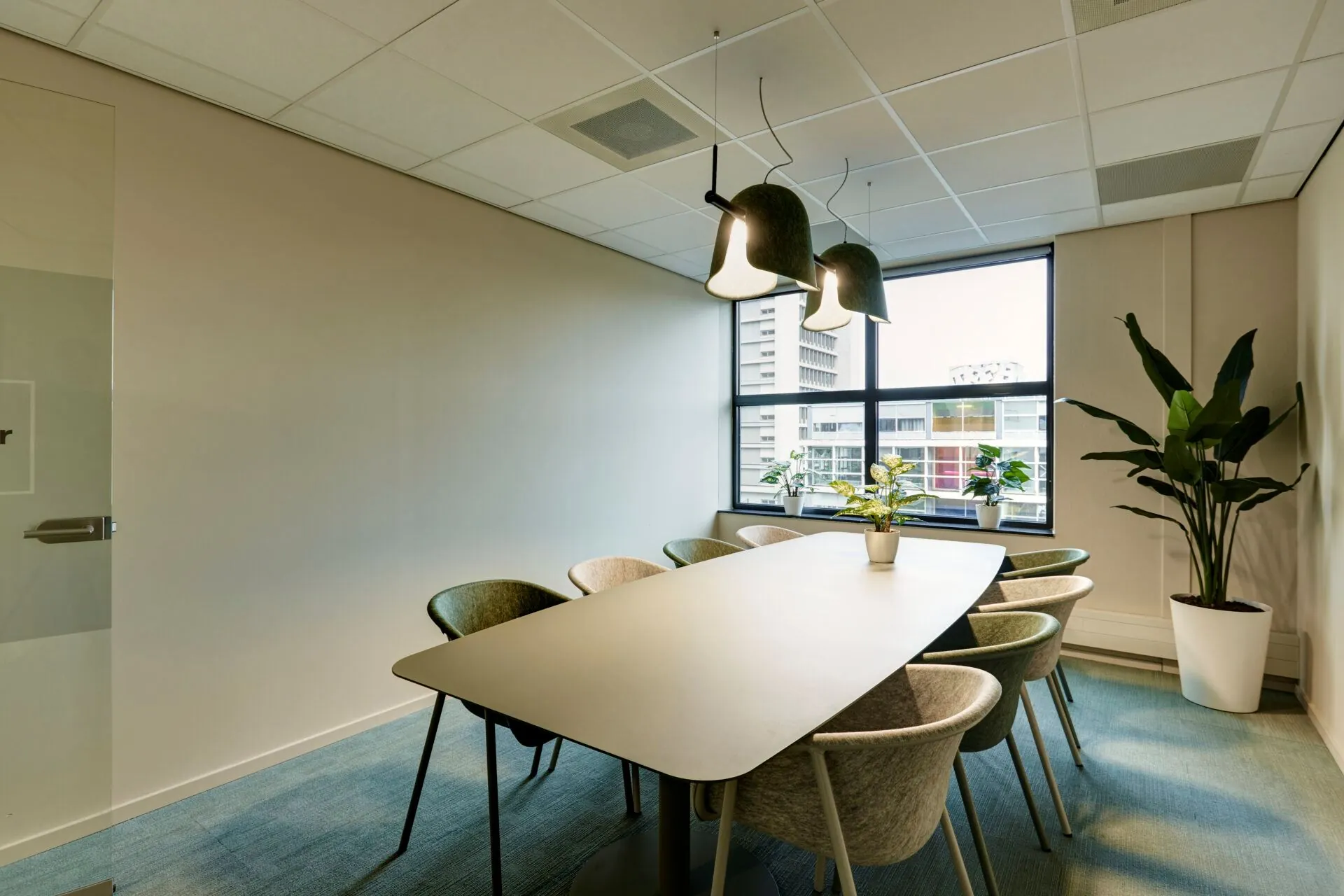 Vergaderruimte met ovale tafel, zes stoelen, moderne verlichting en grote ramen in kantoor Weena 335.