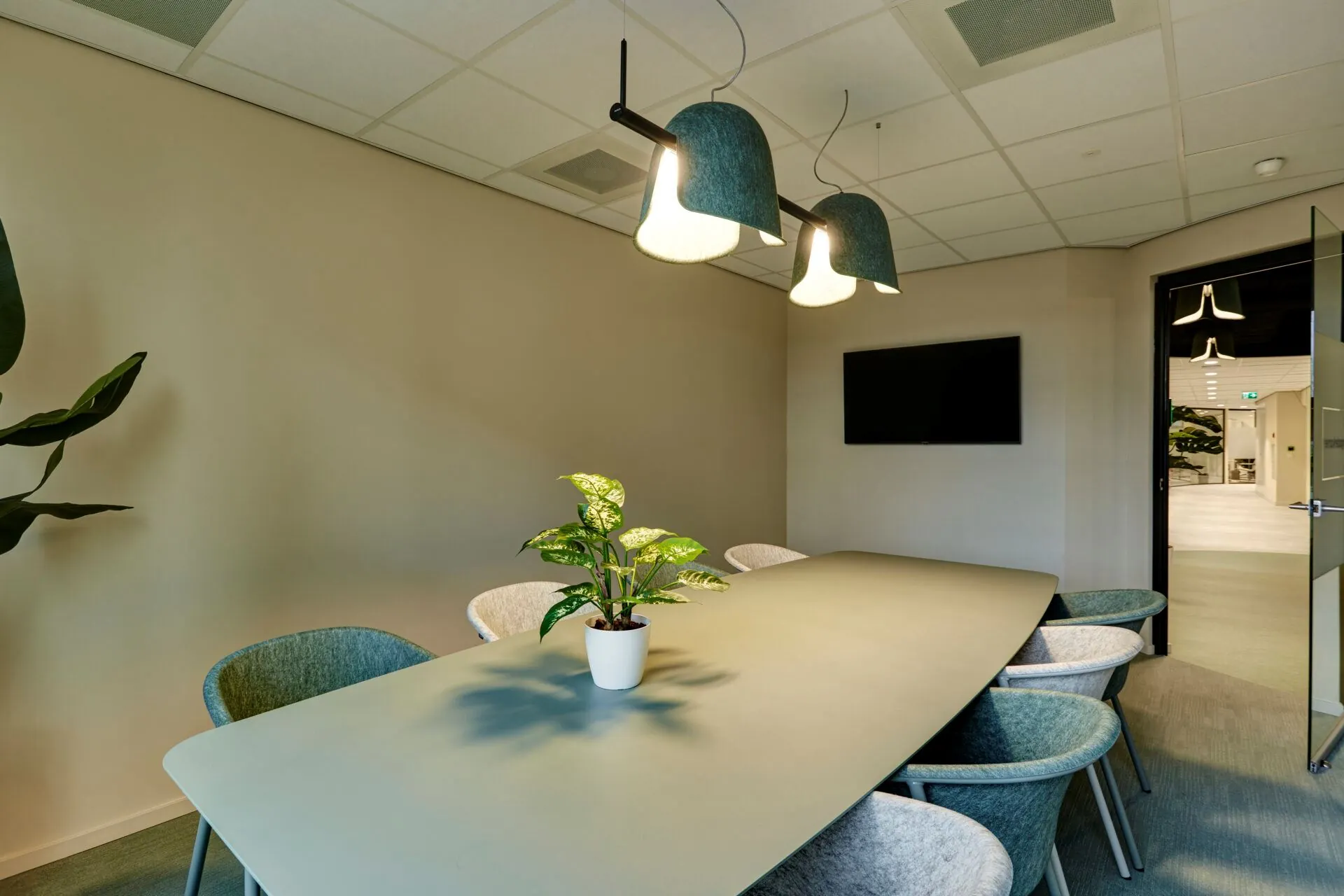 Vergaderruimte Weena 335 met een ovale tafel, acht stoelen, een plant in het midden en een flatscreen aan de muur.