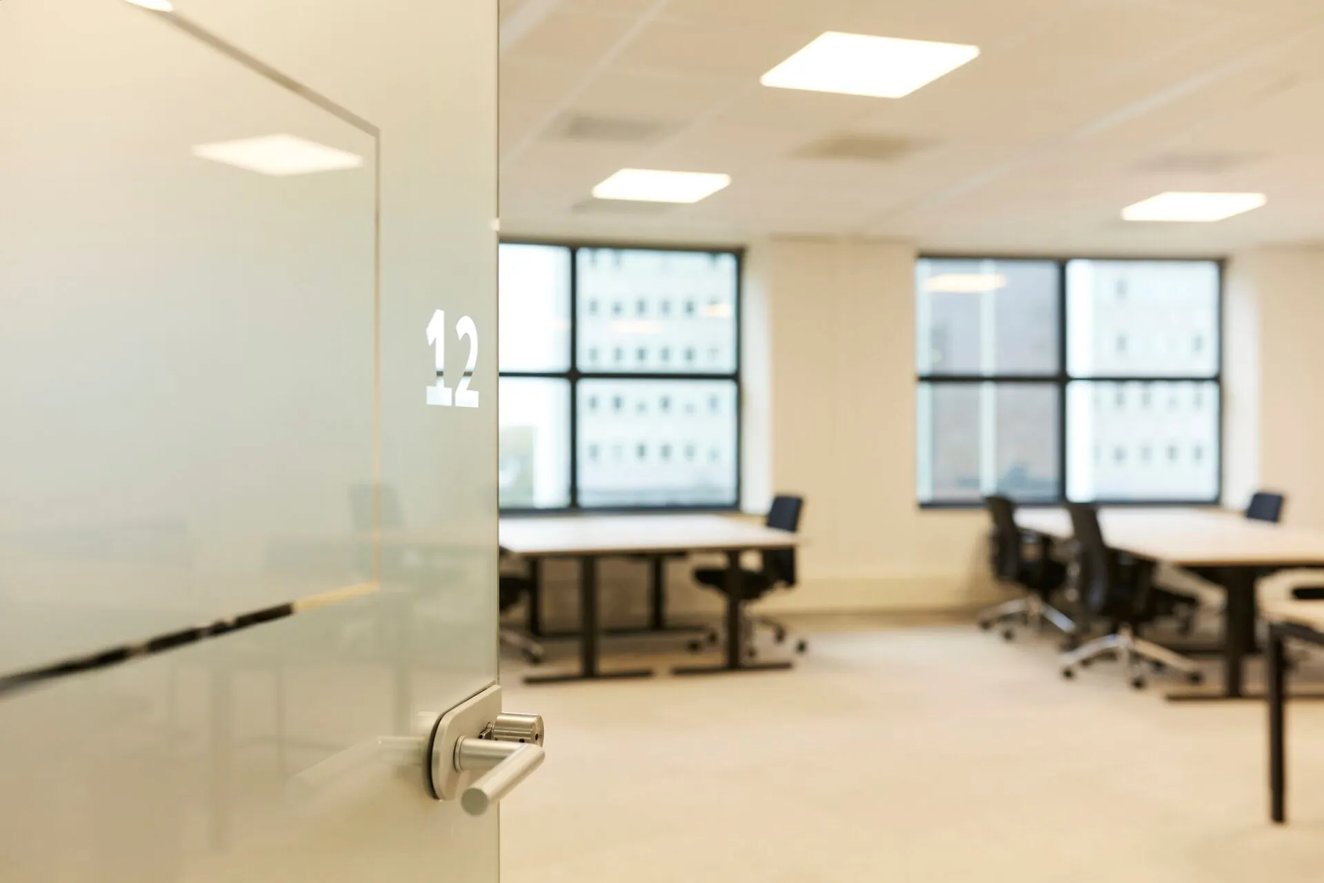 Glazen deur met kamernummer 12 geeft toegang tot een modern, licht kantoor met bureaus en bureaustoelen in Weena 335.