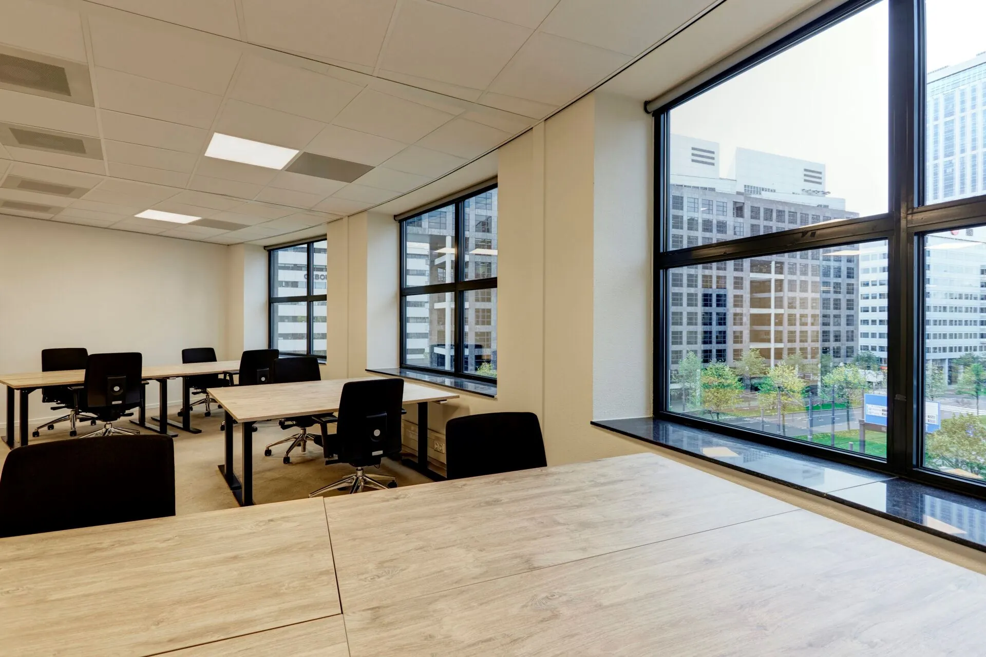 Modern kantoor met meerdere bureaus en bureaustoelen, gelegen aan Weena 335 met uitzicht op kantoorgebouwen in het centrum van Rotterdam.