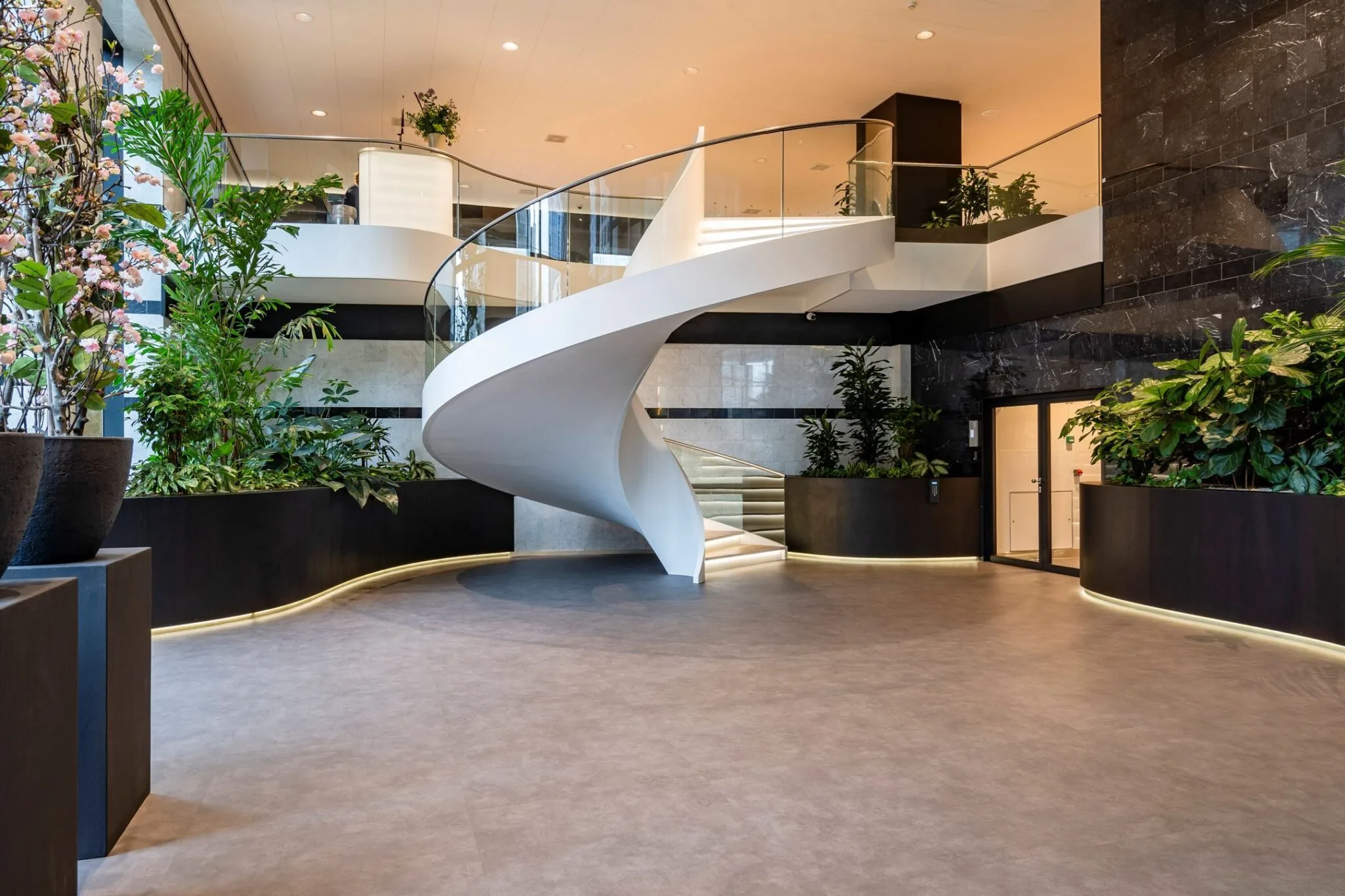 Moderne entreehal van Weena 335 met een witte, spiraalvormige trap en veel groenvoorziening.
