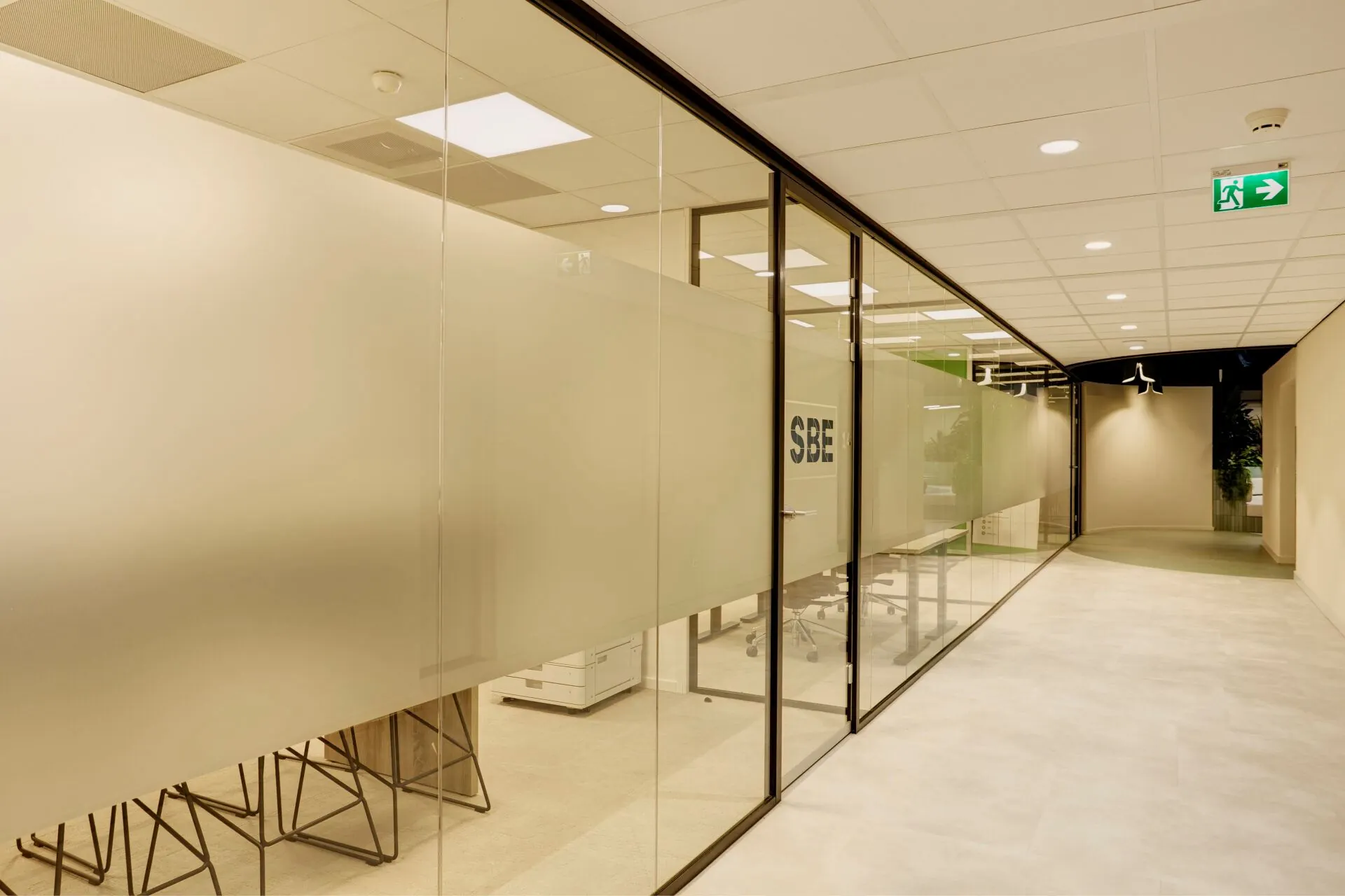 Moderne kantoorgang met glazen wanden en het logo 'SBE' op een deur bij Weena 335.