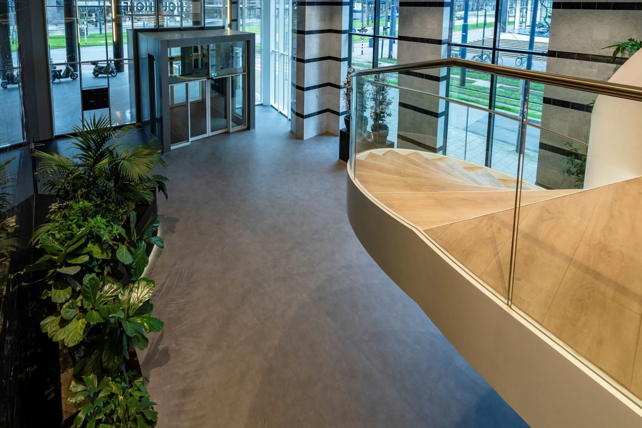 Moderne entreehal van Weena 335 met glazen draaideur, houten trap en groene planten.