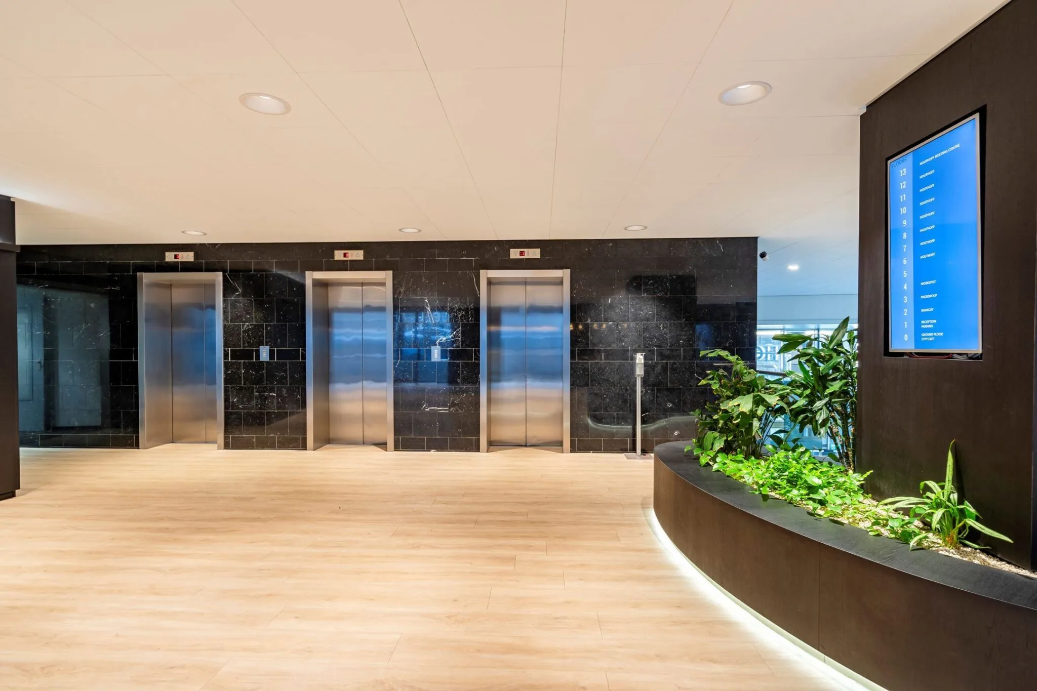 Moderne liftlobby in Weena 335 met drie liften, een digitale verdiepingwijzer en een plantenbak.
