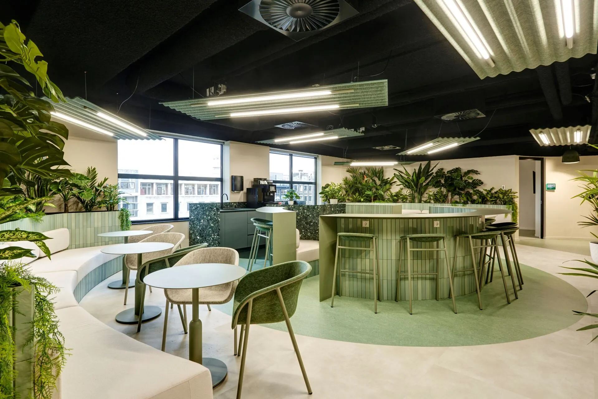 Moderne groene lounge- en werkruimte in Weena 335 met ronde zitplaatsen, planten en een bar met barkrukken.