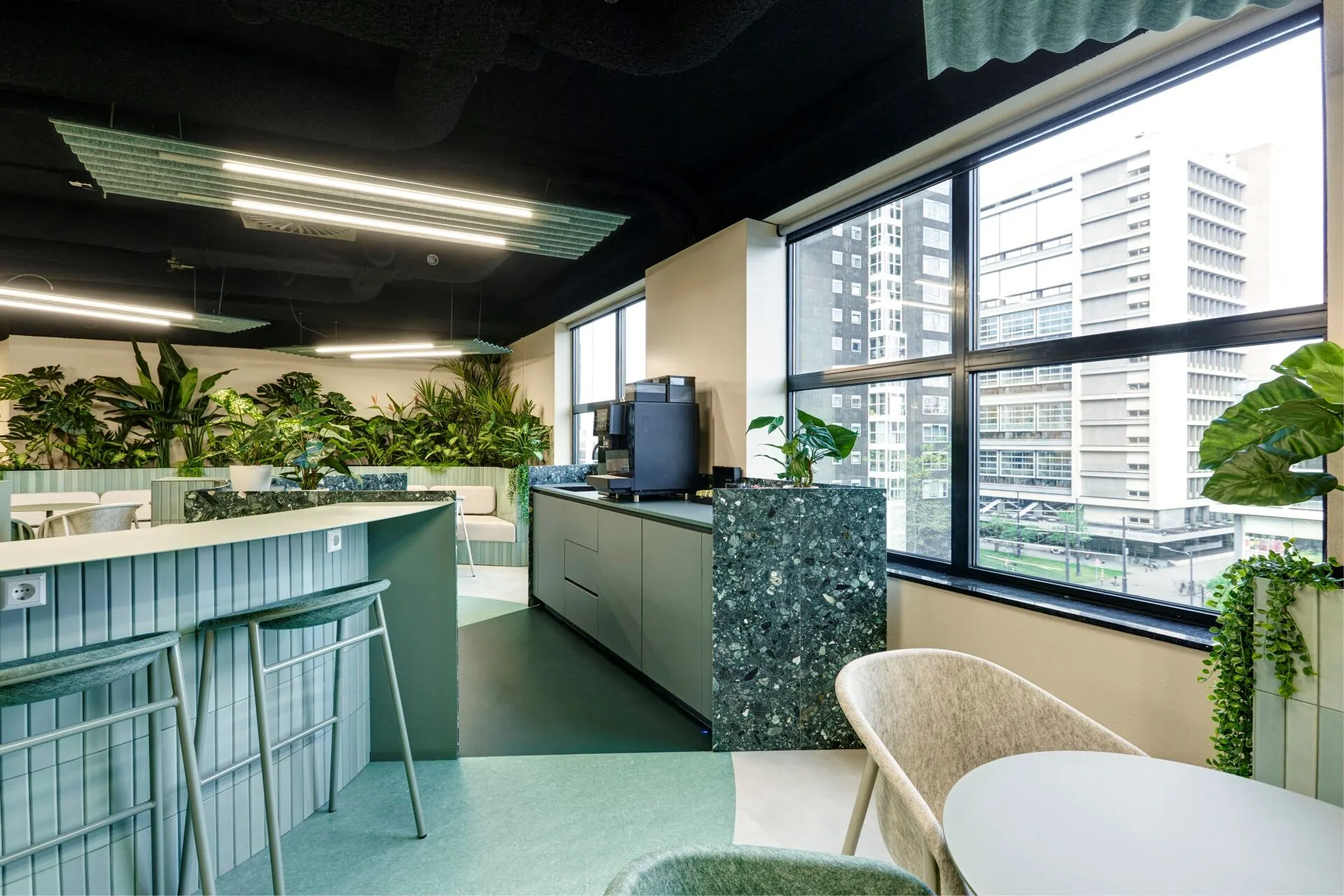 Moderne kantoorlounge op Weena 335 met groen interieur, grote ramen en uitzicht op Rotterdamse hoogbouw.