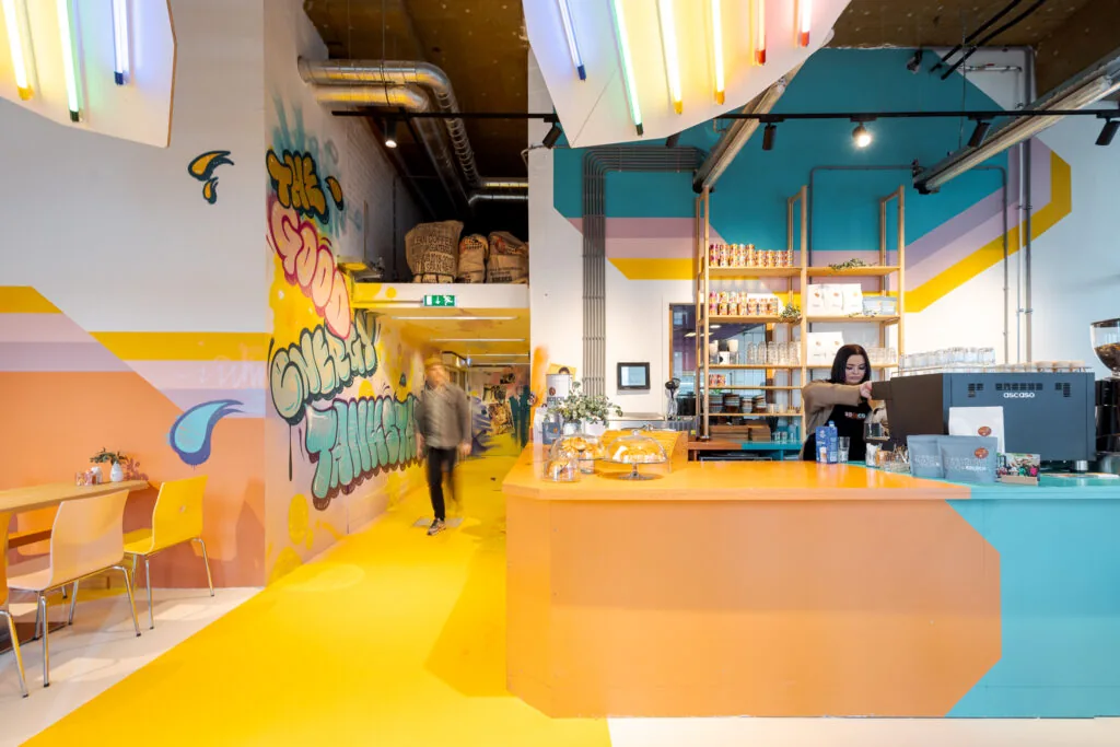 Kleurrijke koffiebar aan de Weena 70 met graffitiwand, moderne inrichting en een barista achter de toonbank.