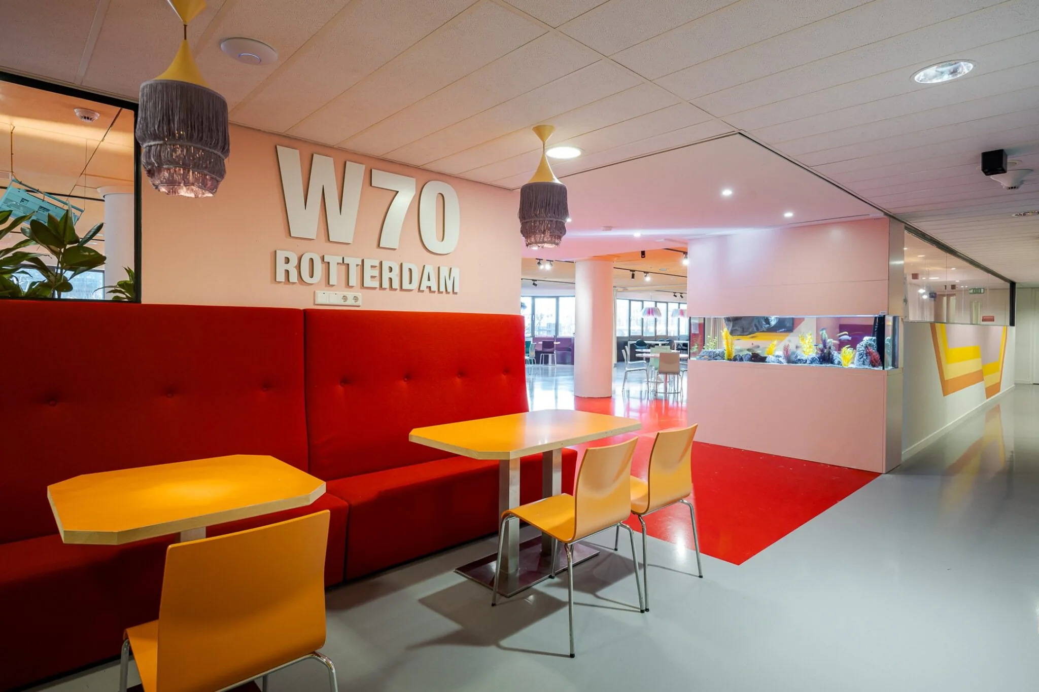 Moderne zithoek met felgekleurde meubels en grote W70 Rotterdam-muuraanduiding in een kantoorgebouw.