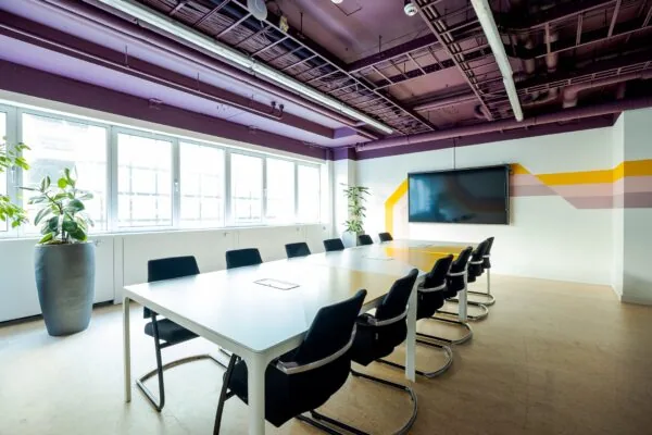 Vergaderruimte in Weena 70 met lange tafel, moderne stoelen, groot scherm en kleurrijk design op de muur.