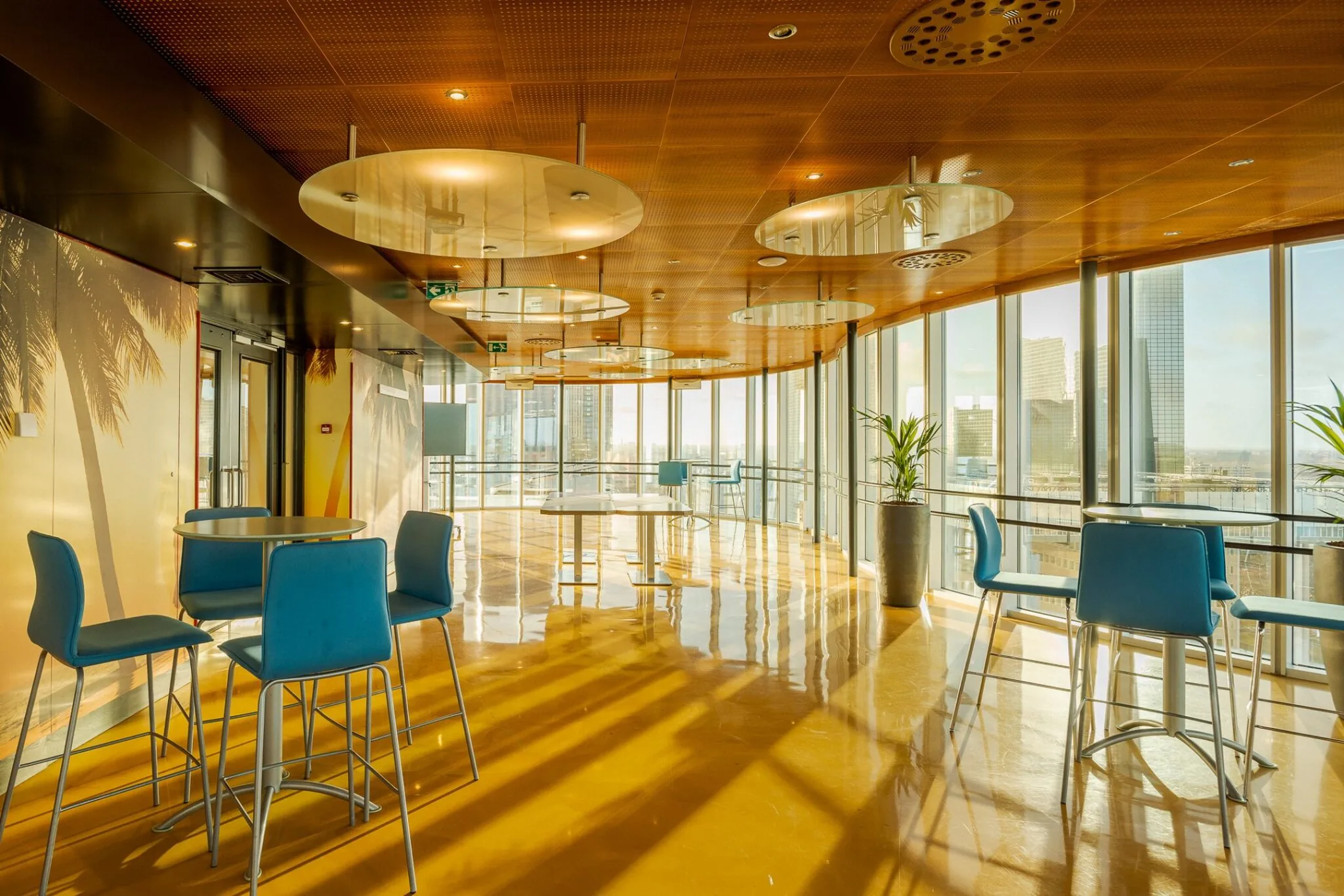 Moderne lounge- of kantineruimte in Weena 70 met blauwe stoelen, ronde tafels en uitzicht op de skyline van Rotterdam.