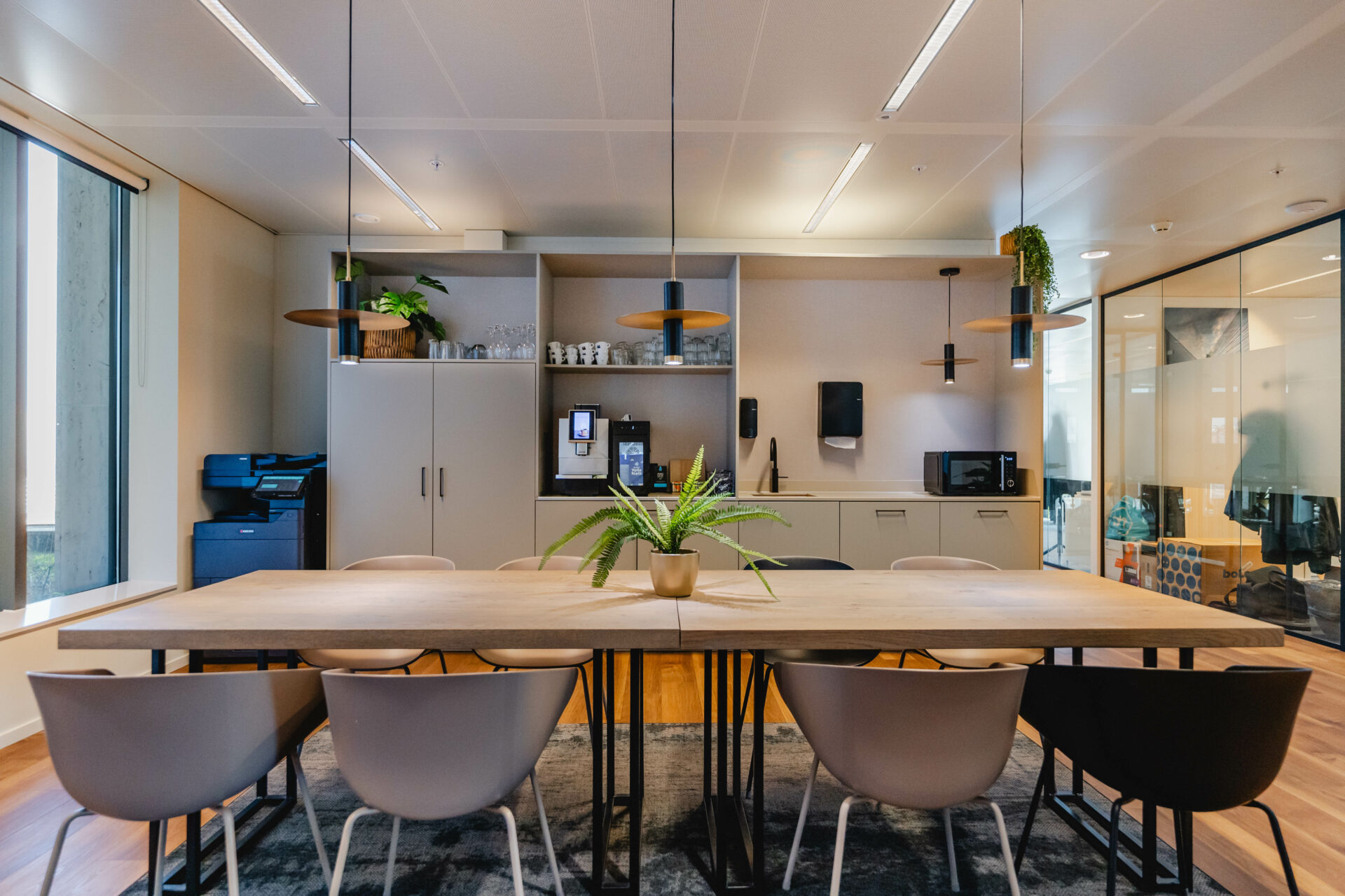Een moderne kantoorruimte met een keukentafel, stoelen en een koffiezetapparaat.