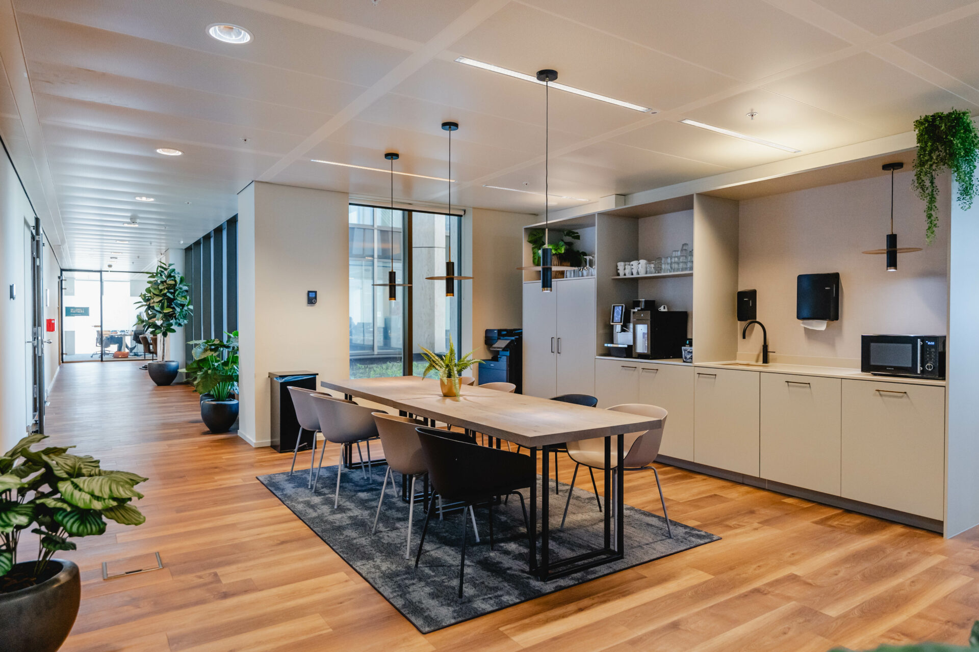 Een moderne kantoorruimte met een lange houten tafel, omgeven door stoelen en voorzien van een kitchenette aan de zijkant.