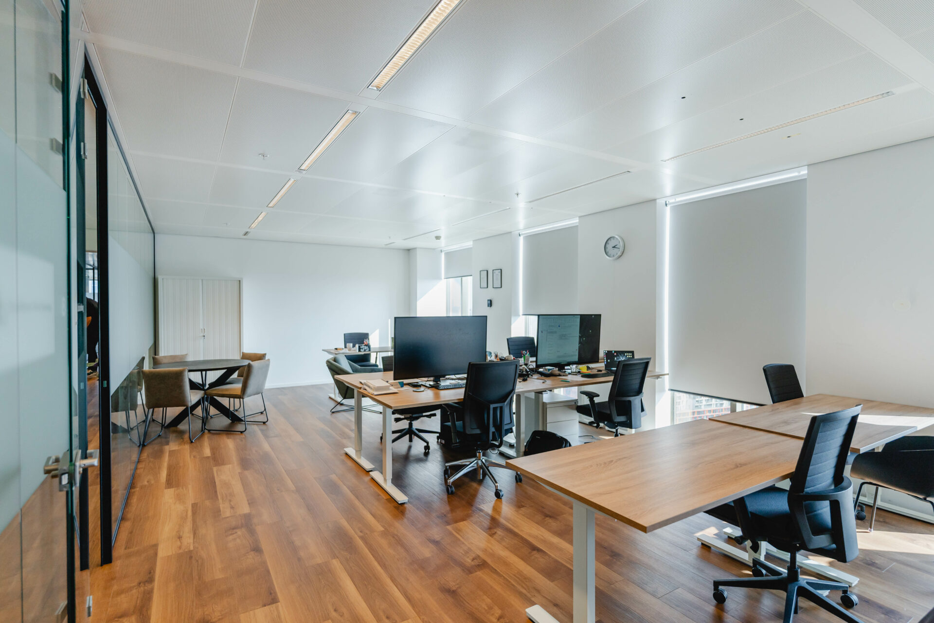Een moderne, lichte kantoorruimte met bureaus, stoelen en computers.