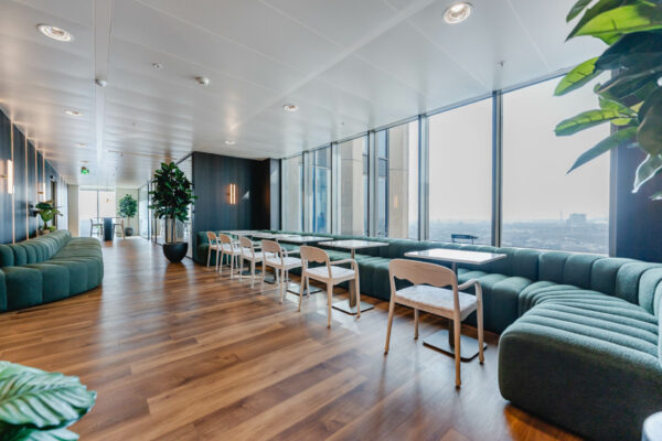 Een moderne kantoorruimte met glazen ramen, groene banken en houten vloeren.