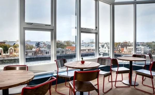 Moderne zithoek met houten tafels en stoelen bij grote ramen met uitzicht op Amsterdam vanaf Weesperstraat 61-105.