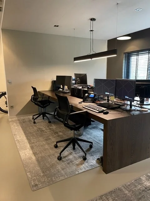 Moderne werkplek met bureaus, bureaustoelen, computers en kantoorartikelen in een net ingerichte kantoorruimte.