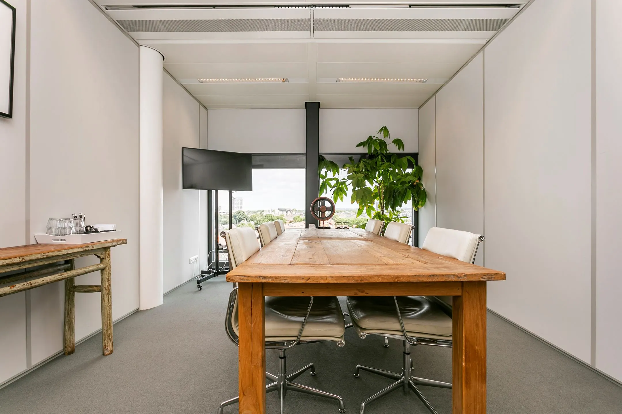 Vergaderruimte met een houten tafel, witte stoelen, een grote plant en een flatscreen, gelegen aan het Wim Duisenbergplantsoen 31.