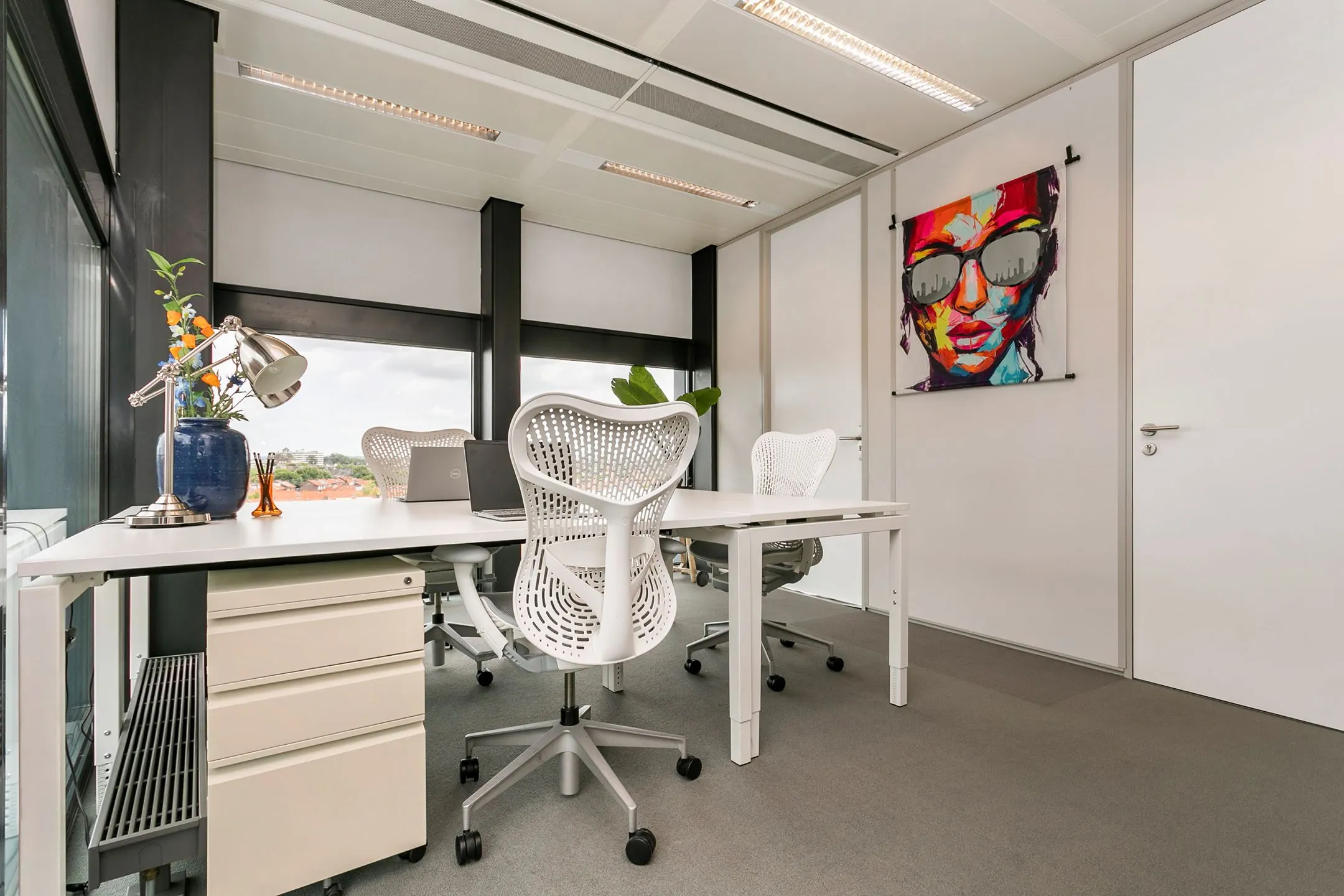 Modern kantoorinterieur op Wim Duisenbergplantsoen 31 met witte bureaus, designstoelen en kleurrijke muurschildering.
