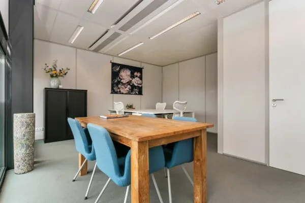 Kantoorruimte met houten vergadertafel, blauwe stoelen en een werkplek in een moderne, lichte inrichting aan het Wim Duisenbergplantsoen.