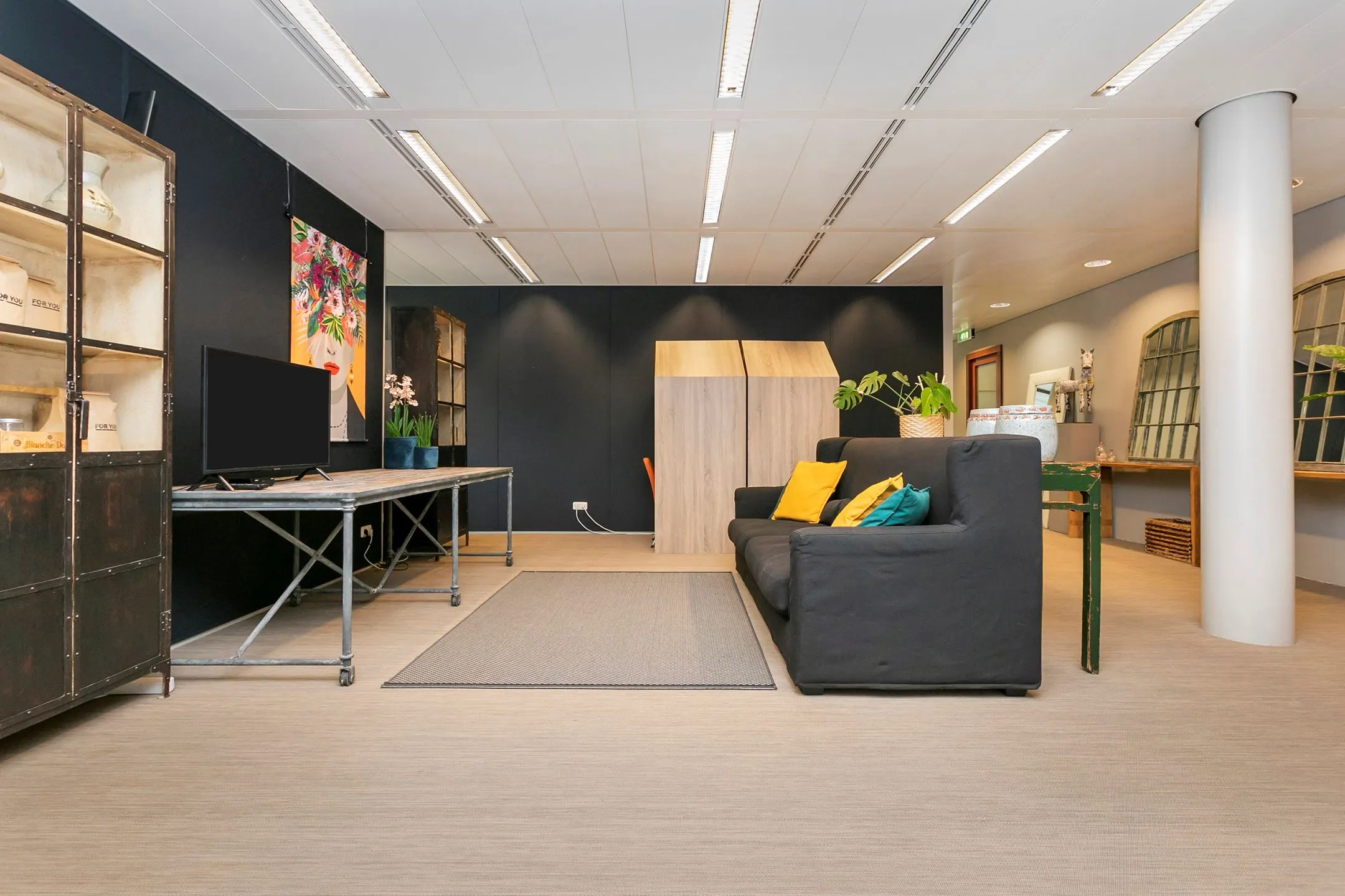 Modern ingerichte wachtruimte met een zwarte bank, gekleurde kussens, planten en industriële accenten aan het Wim Duisenbergplantsoen 31.