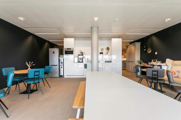 Moderne kantoorkeuken met zithoeken, een lange tafel en witte kastenwand op Wim Duisenbergplantsoen 31.