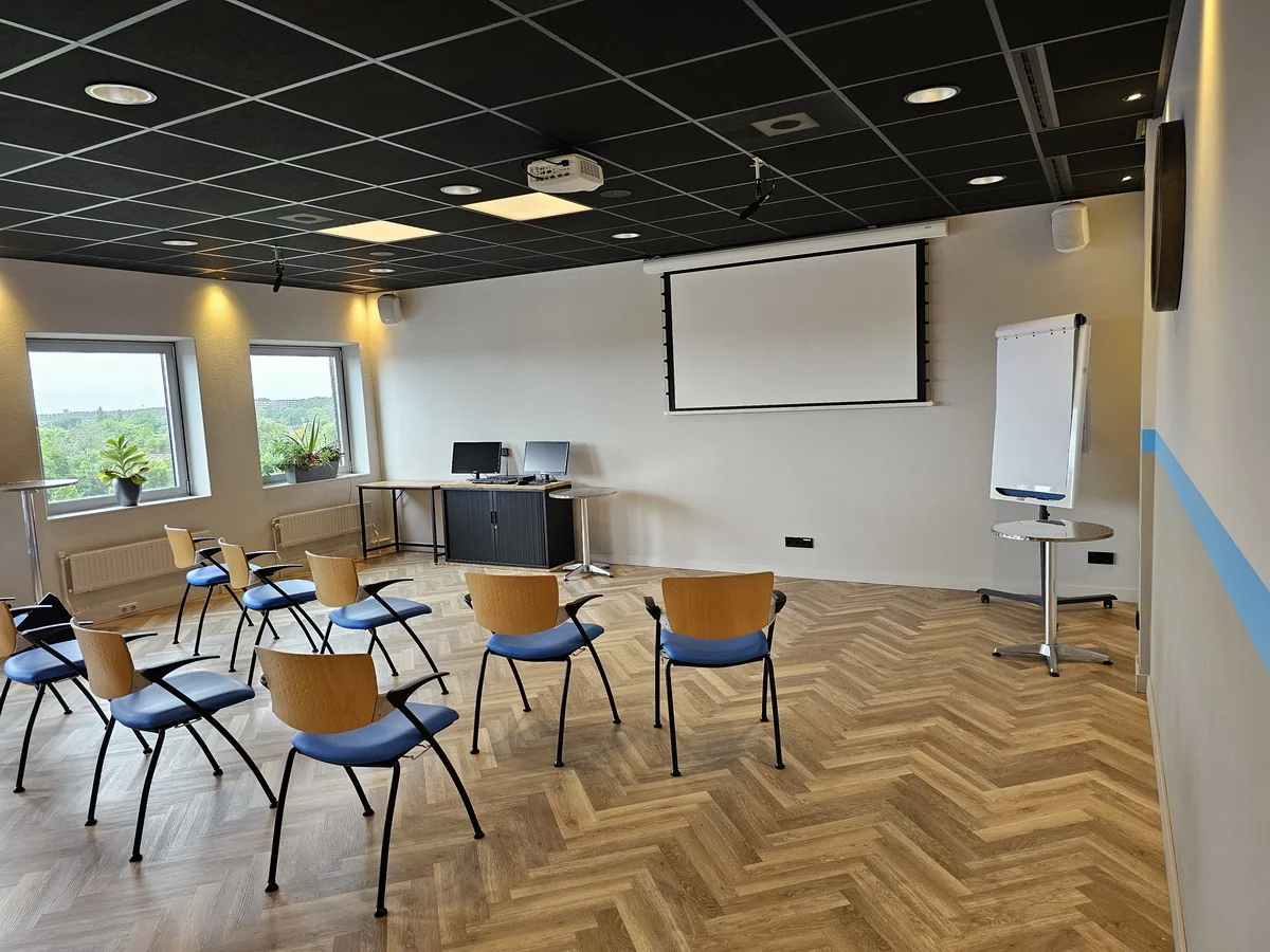 Vergaderruimte Zaal3 met stoelen in opstelling, een projector, flip-over en werktafel bij het raam.