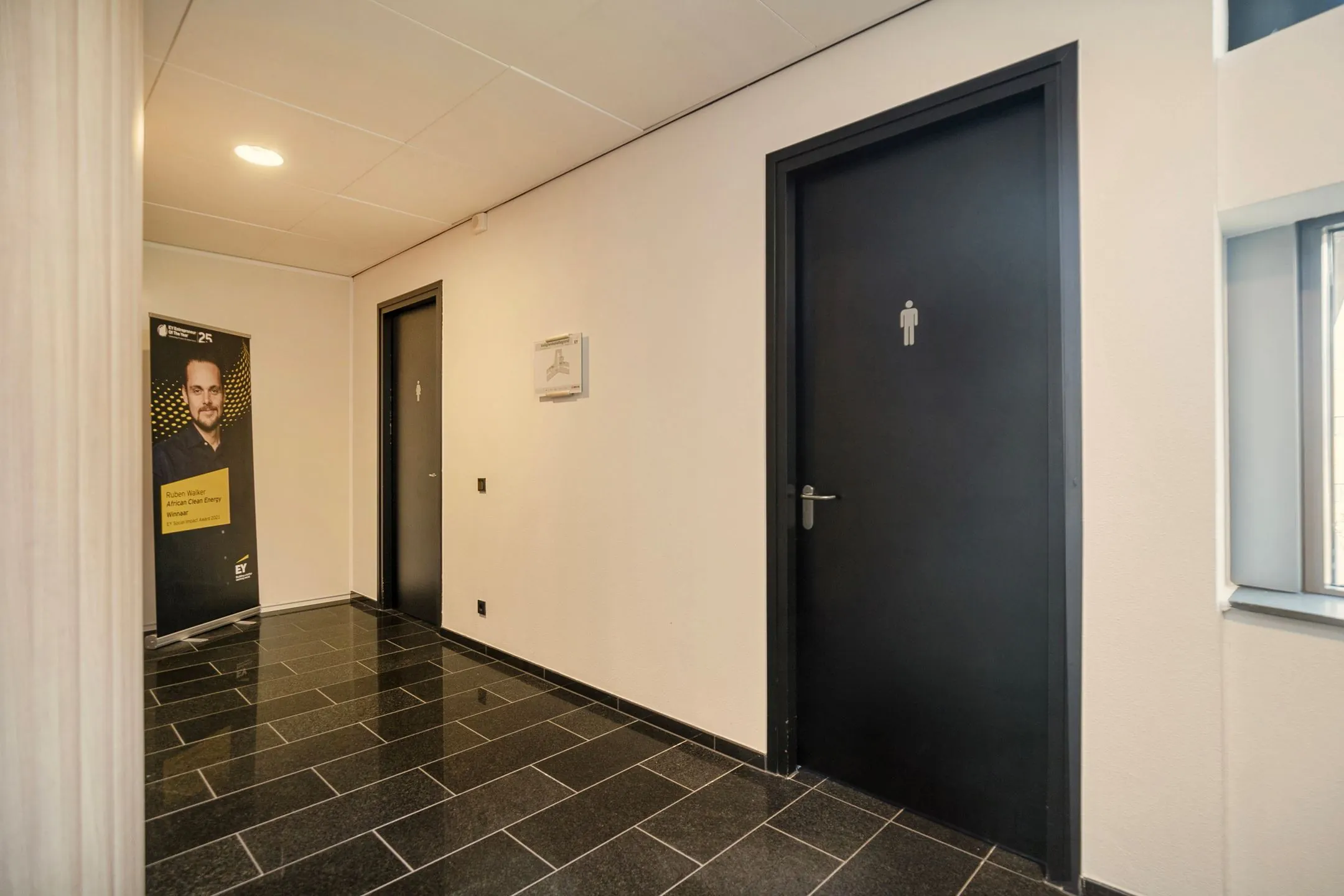 Gang met zwarte tegelvloer, twee toiletten en een banner van Ruben Karel bij Zwartewaterallee 56.