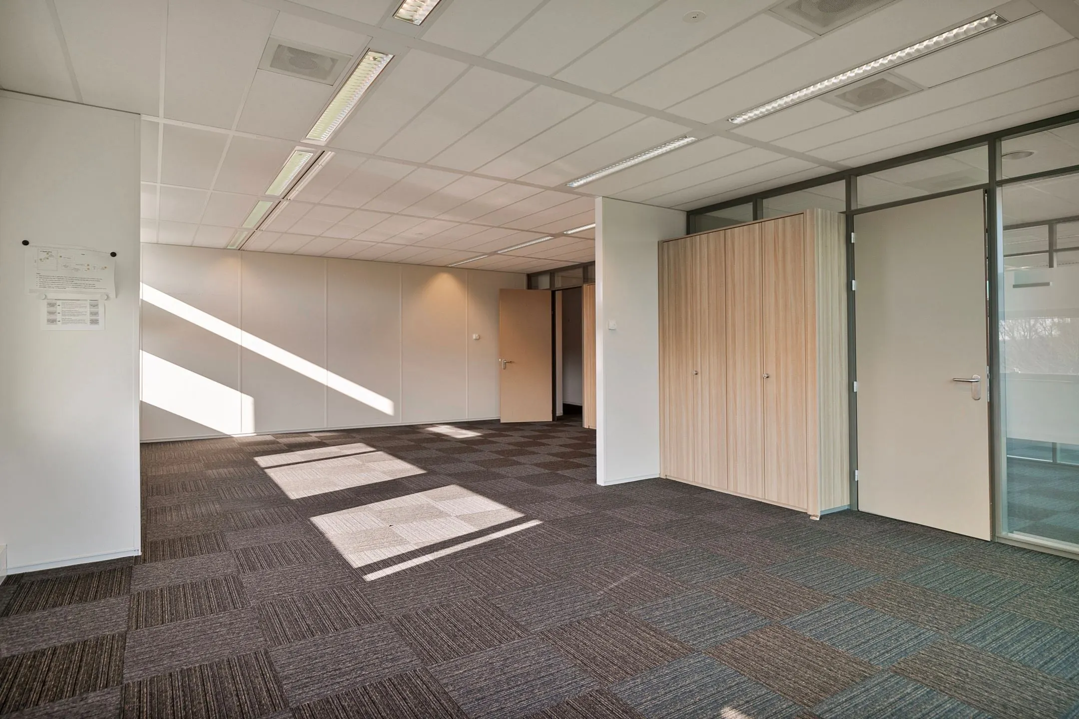 Leeg en modern kantoorruimte met tapijttegels, systeemplafond en ingebouwde kasten aan de Zwartewaterallee 56.