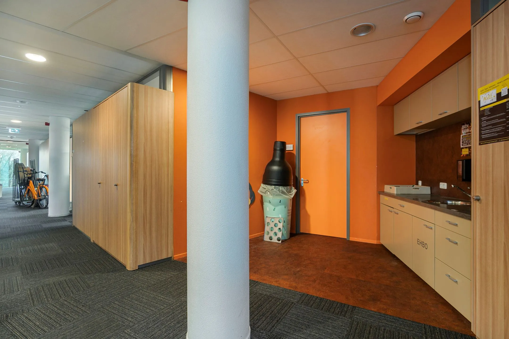 Keukenhoek met oranje muren en EHBO-kast in een gang van Zwartewaterallee 56, met een opvallende prullenbak in de vorm van een ijsje.