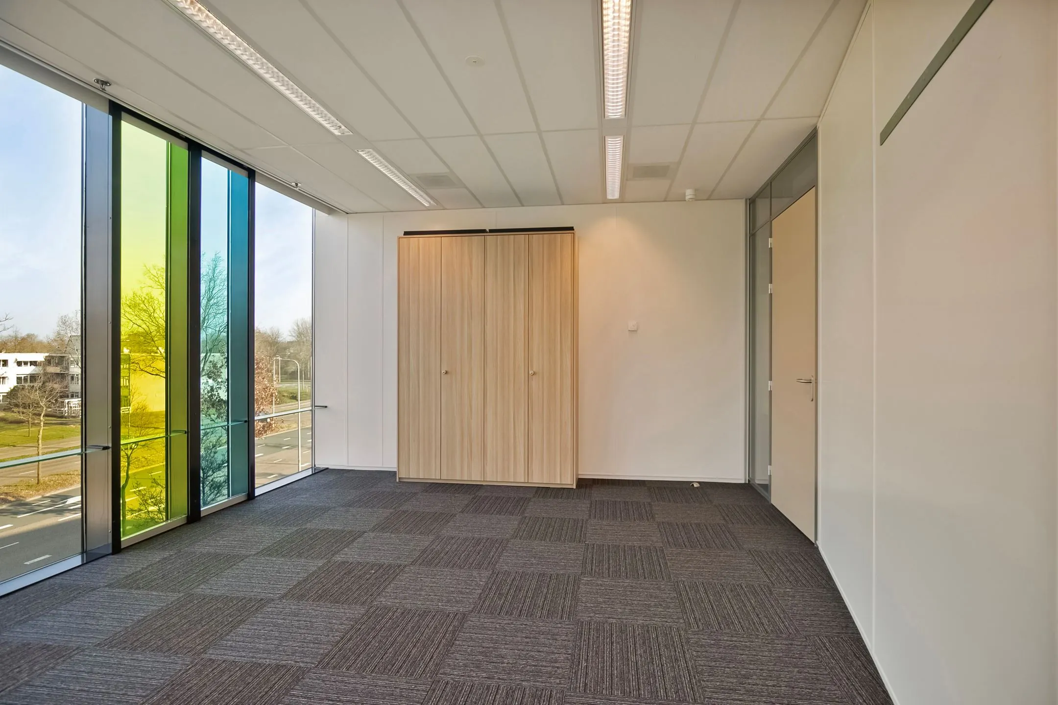 Licht kantoorruimte met gekleurde glazen wand, grijs tapijt en houten opbergkast aan de Zwartewaterallee 56.