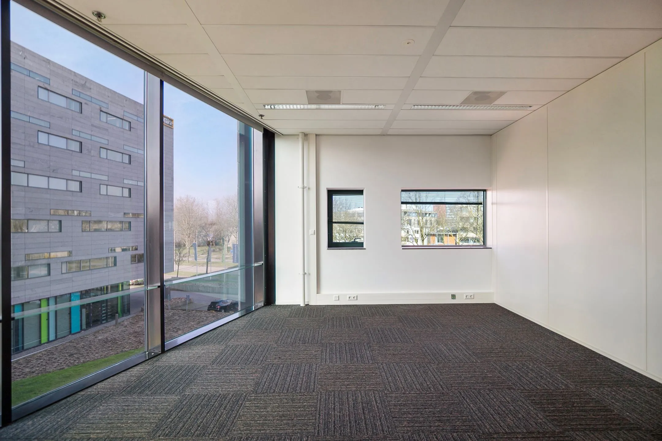 Leeg kantoor met grote ramen en uitzicht op een modern kantoorgebouw aan de Zwartewaterallee.