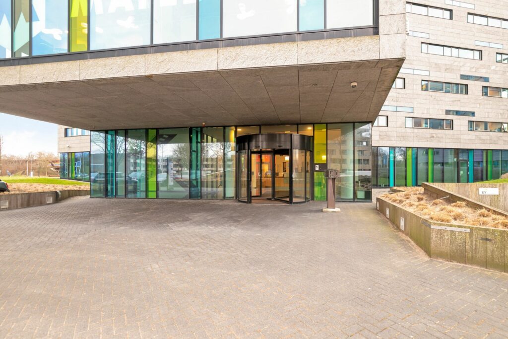 Ingang van het moderne kantoorgebouw aan de Zwartewaterallee 56 met een draaideur en kleurrijke glazen gevel.