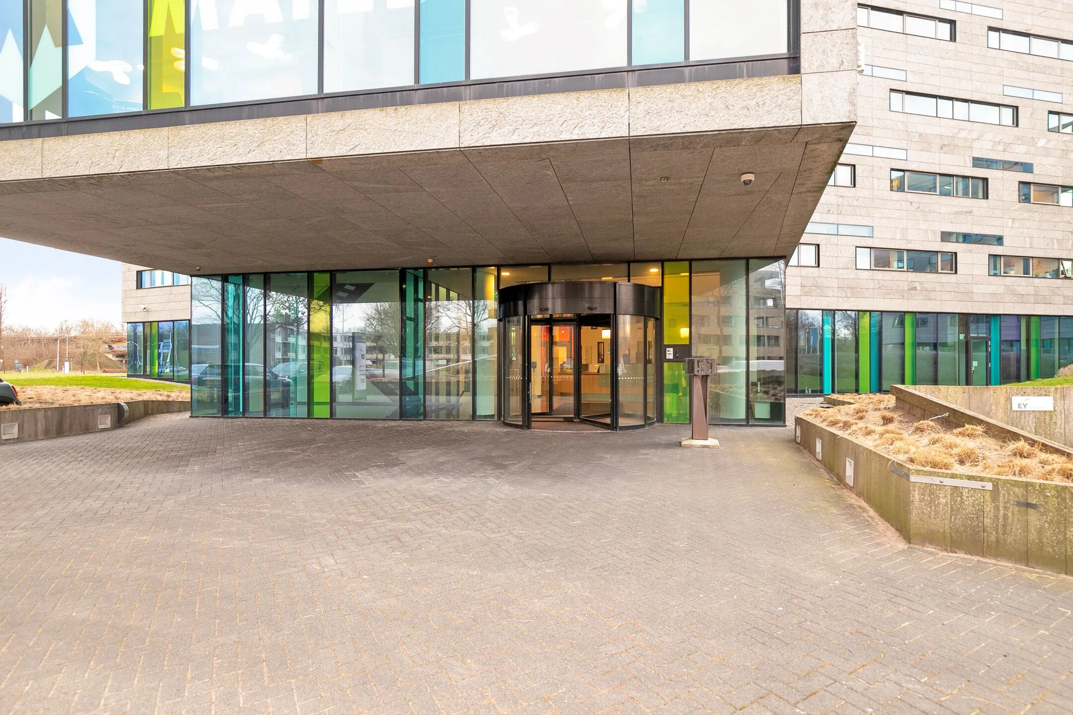Ingang van het moderne kantoorgebouw aan de Zwartewaterallee 56 met een draaideur en kleurrijke glazen gevel.