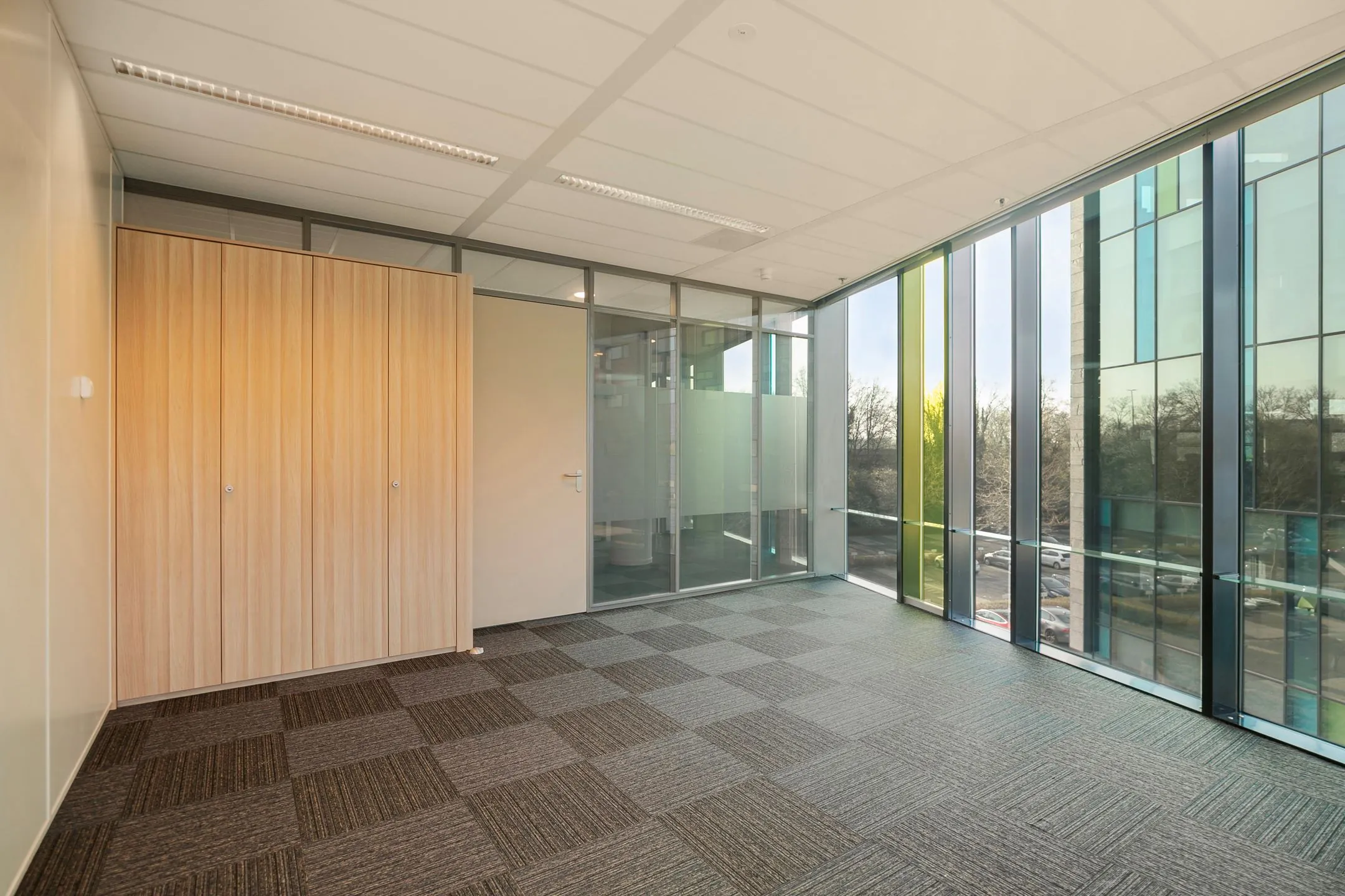 Licht en modern kantoor met glazen wanden, grote raampartijen en een houten kast, gelegen aan de Zwartewaterallee 56.