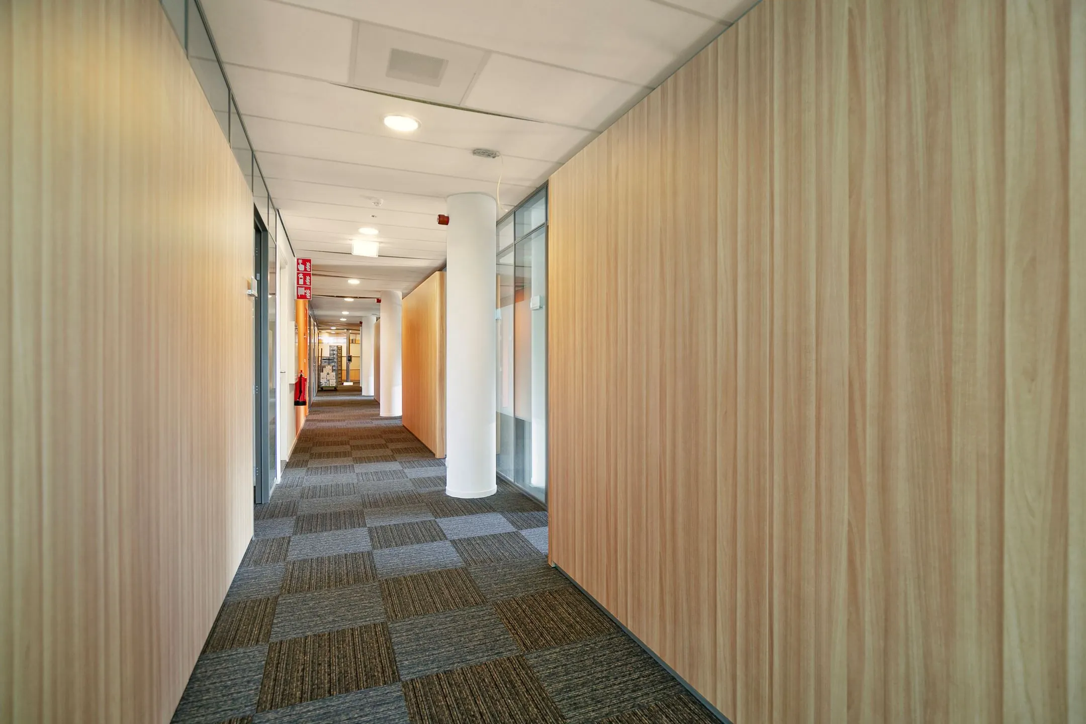 Verlichte gang in een modern kantoorpand aan de Zwartewaterallee 56 met houten wandpanelen en tapijttegels.