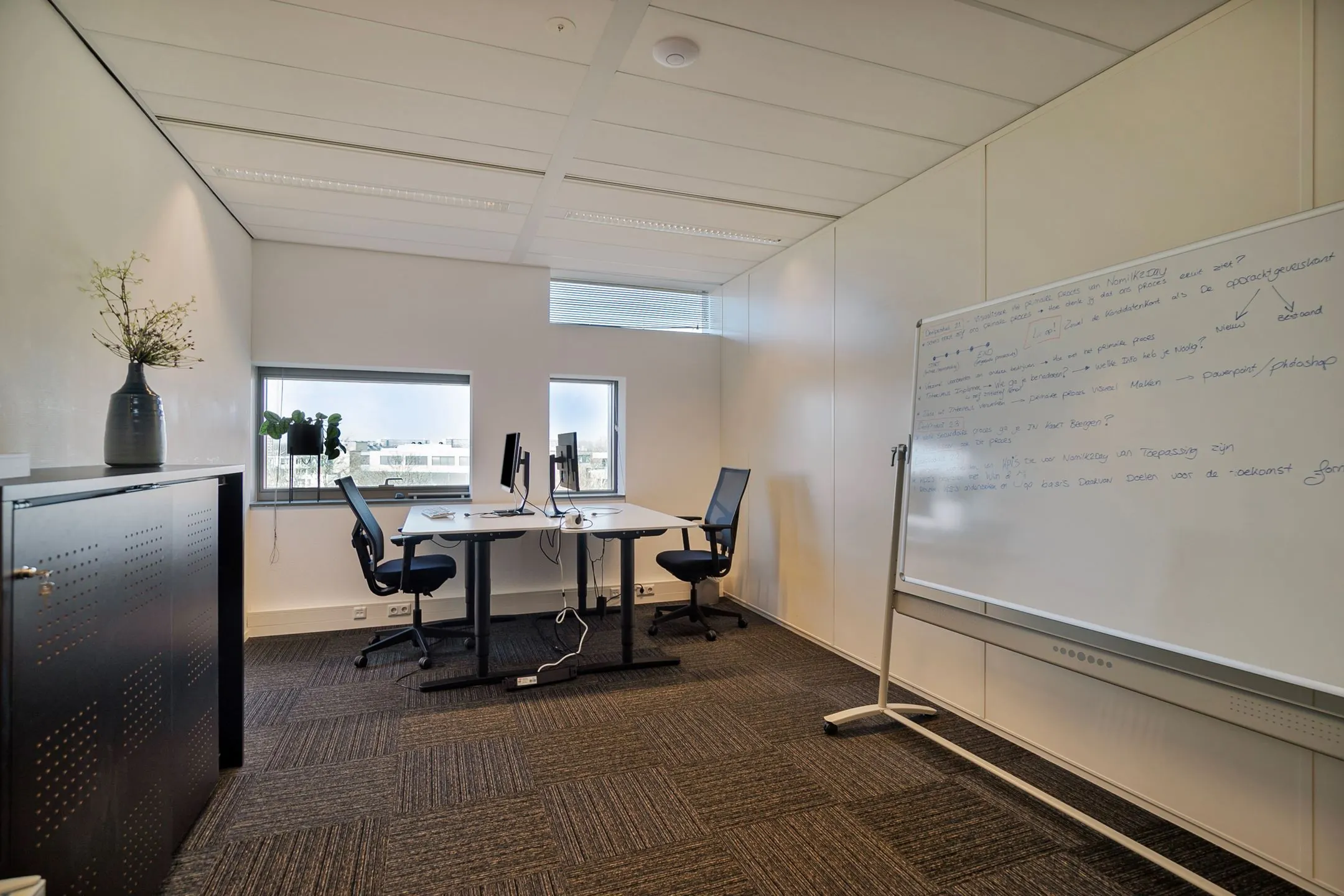 Modern kantoor met twee bureaus, een whiteboard vol aantekeningen en uitzicht op de stad, bij Zwartewaterallee 56.