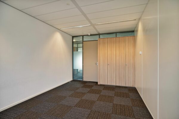 Lege kantoorruimte met tapijttegels, inbouwkast en een deur met glazen zijpaneel aan de Zwartewaterallee 56.