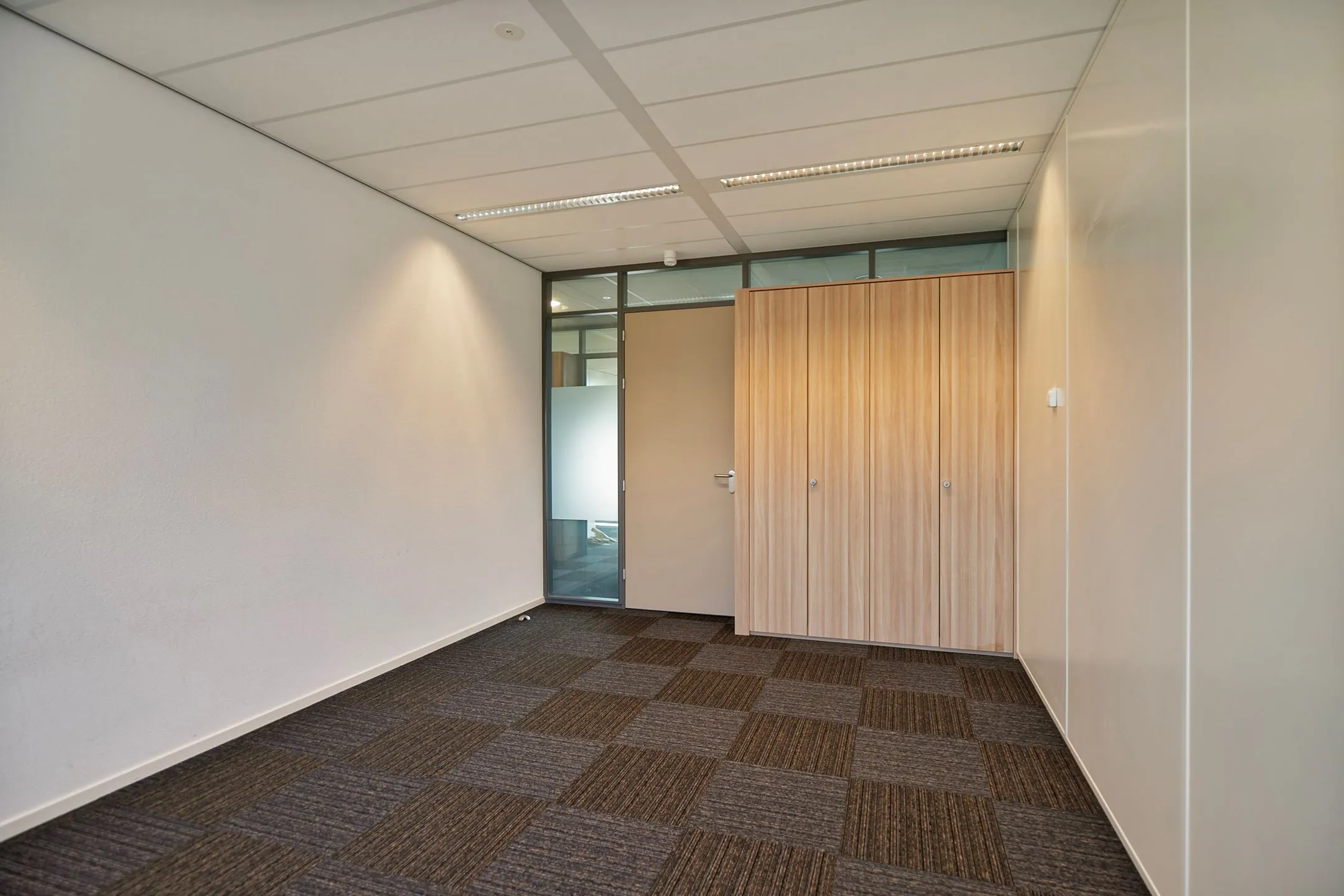 Lege kantoorruimte met tapijttegels, inbouwkast en een deur met glazen zijpaneel aan de Zwartewaterallee 56.
