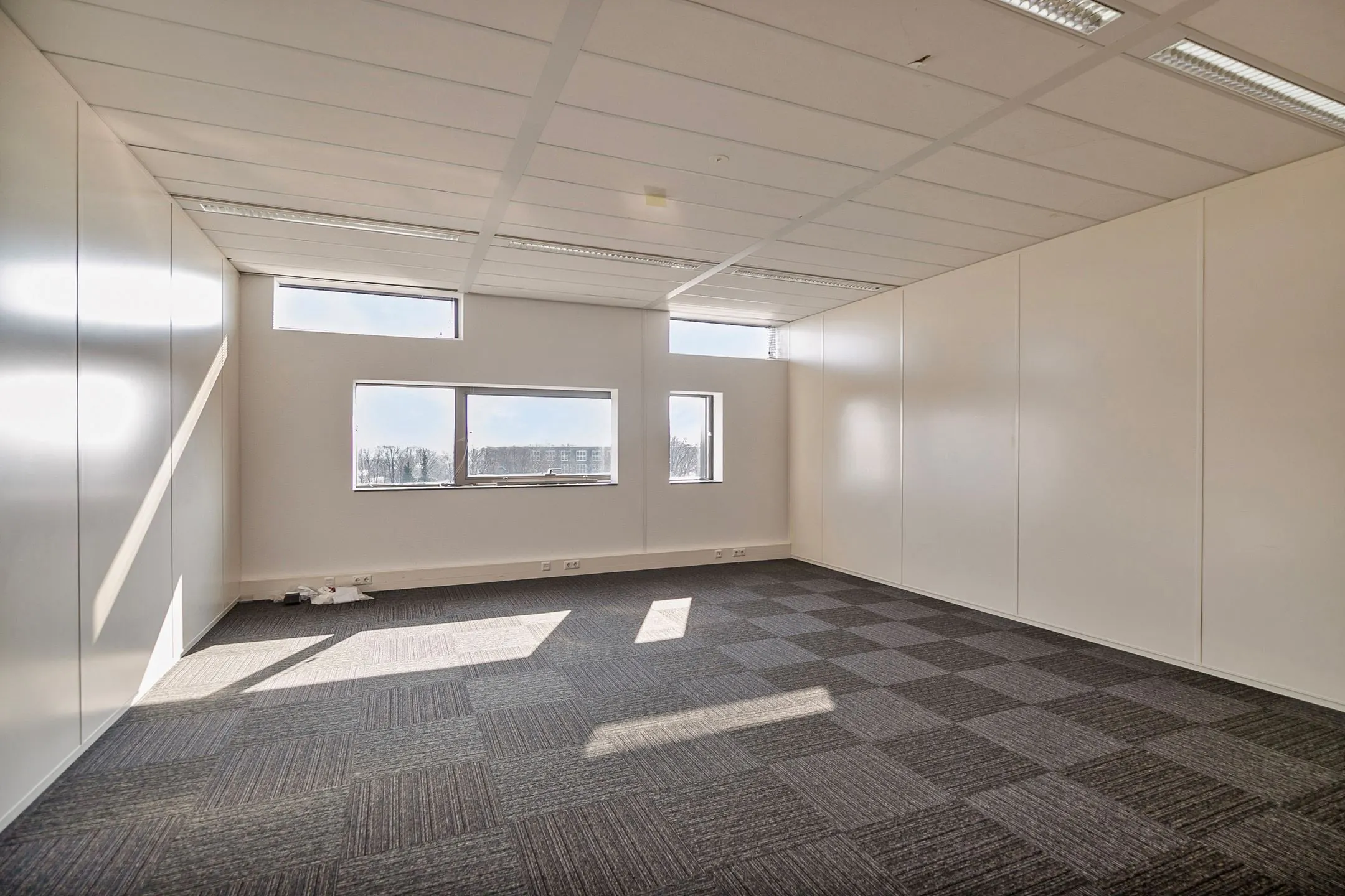 Licht, leeg kantoor met tapijttegels en grote ramen aan de Zwartewaterallee 56.