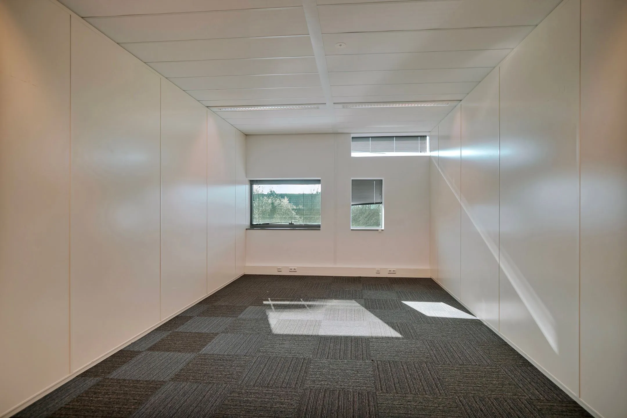 Lege kantoorruimte met tapijttegels, witte wanden en twee ramen aan de achterkant in Zwartewaterallee 56.
